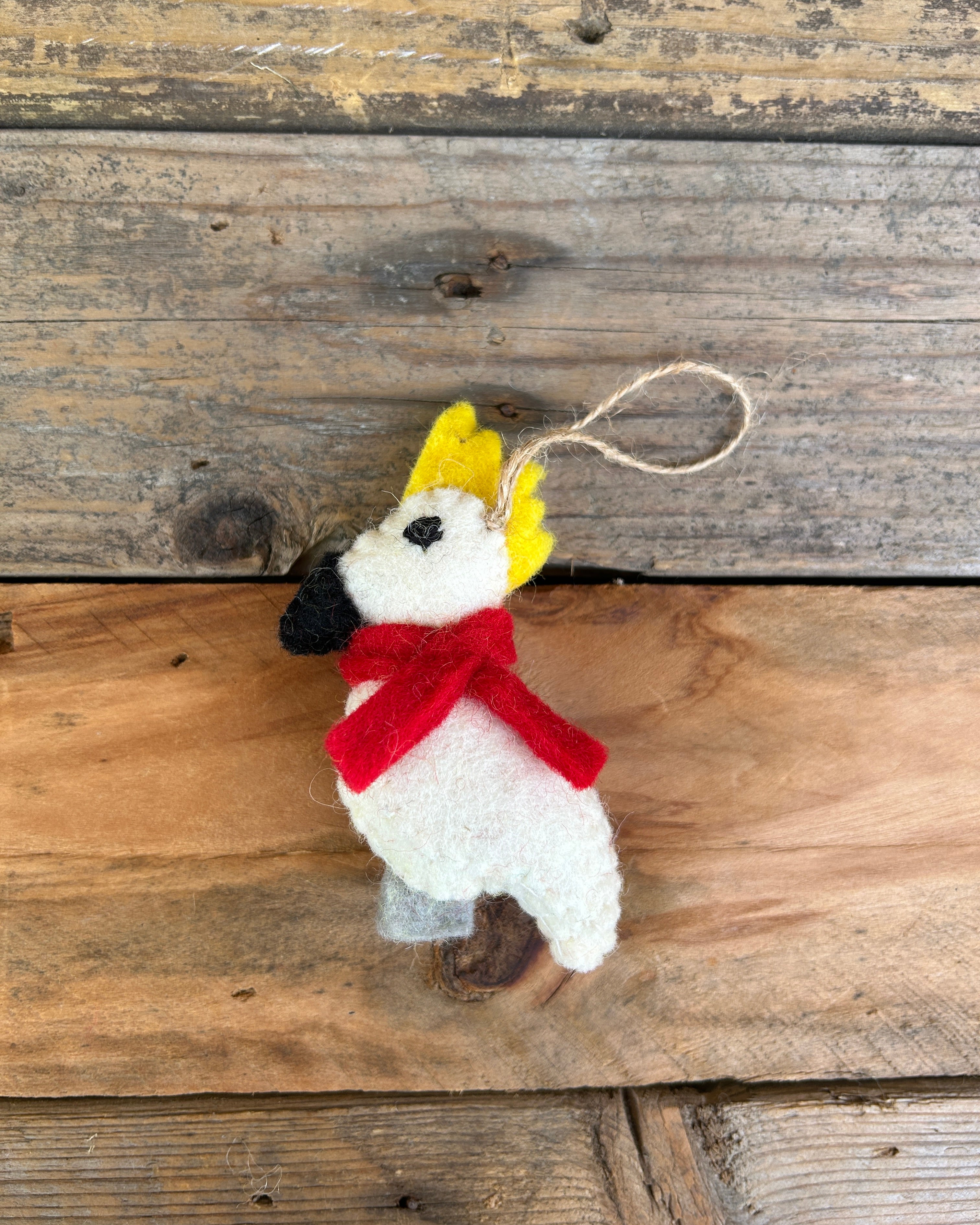 Decorative cockatoo ornament with a red scarf and yellow hat on a wooden surface