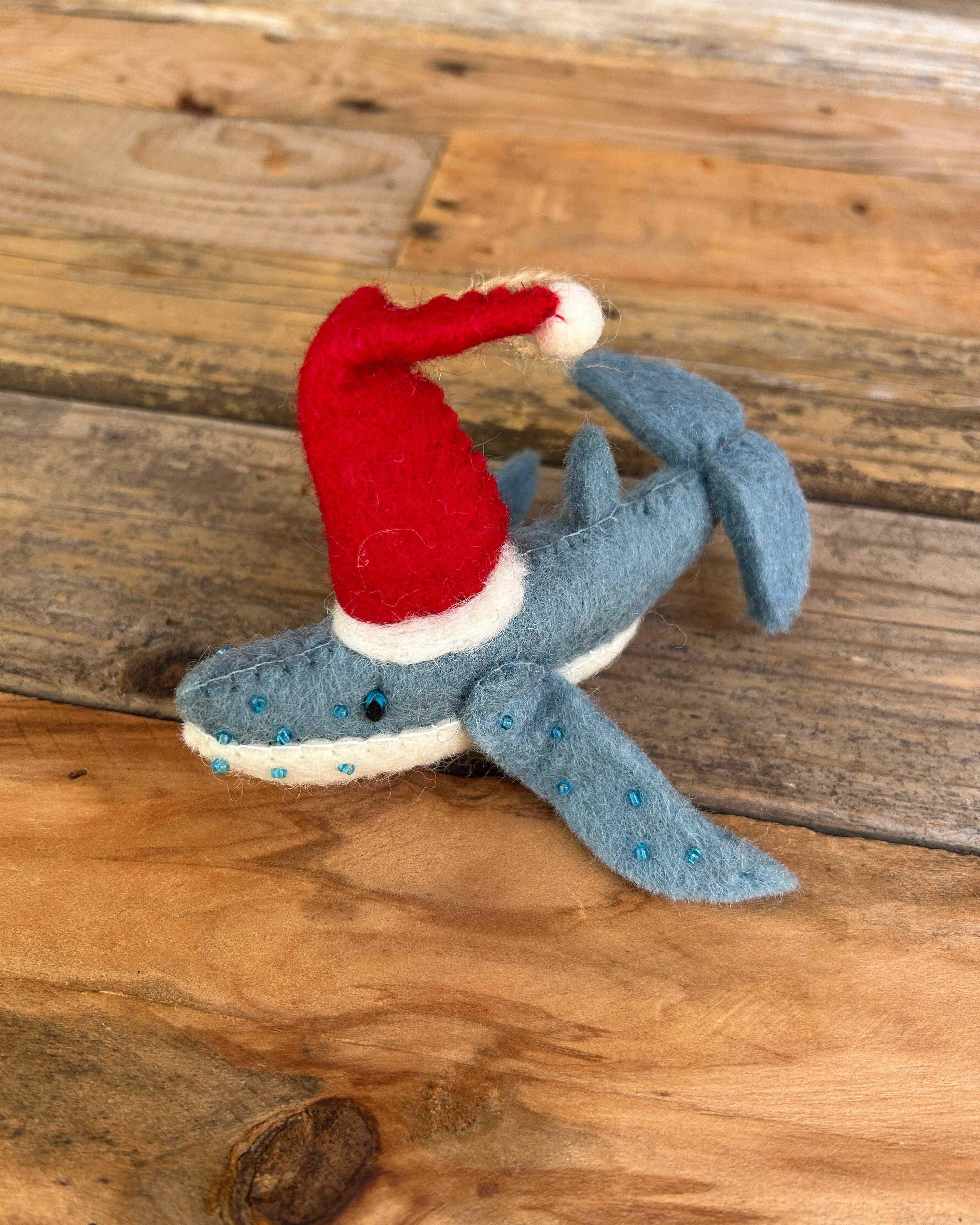 Felt sky gypsies ornament wearing a red Santa hat on a wooden surface