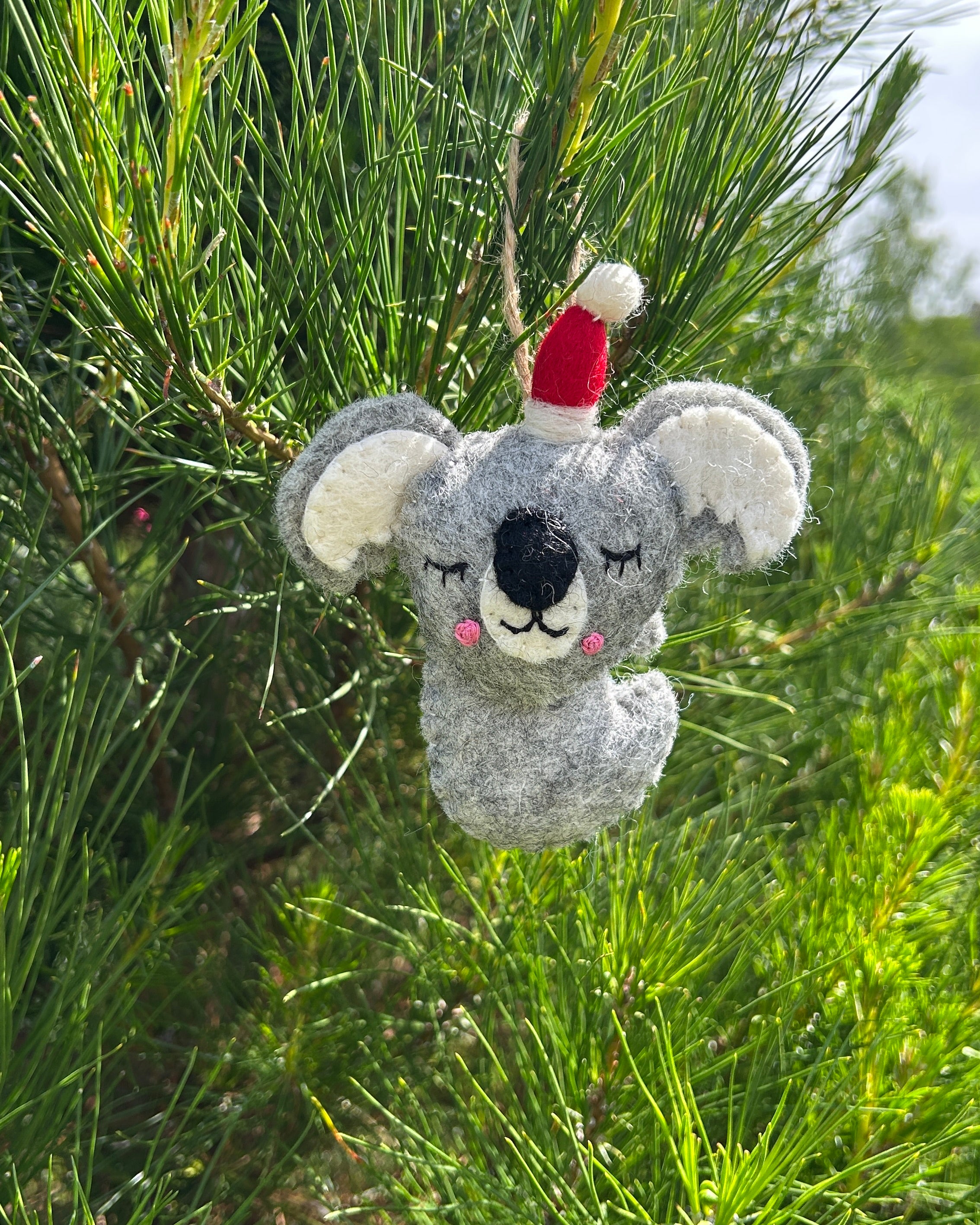 Felt koala ornament with a red hat hanging on a tree branch