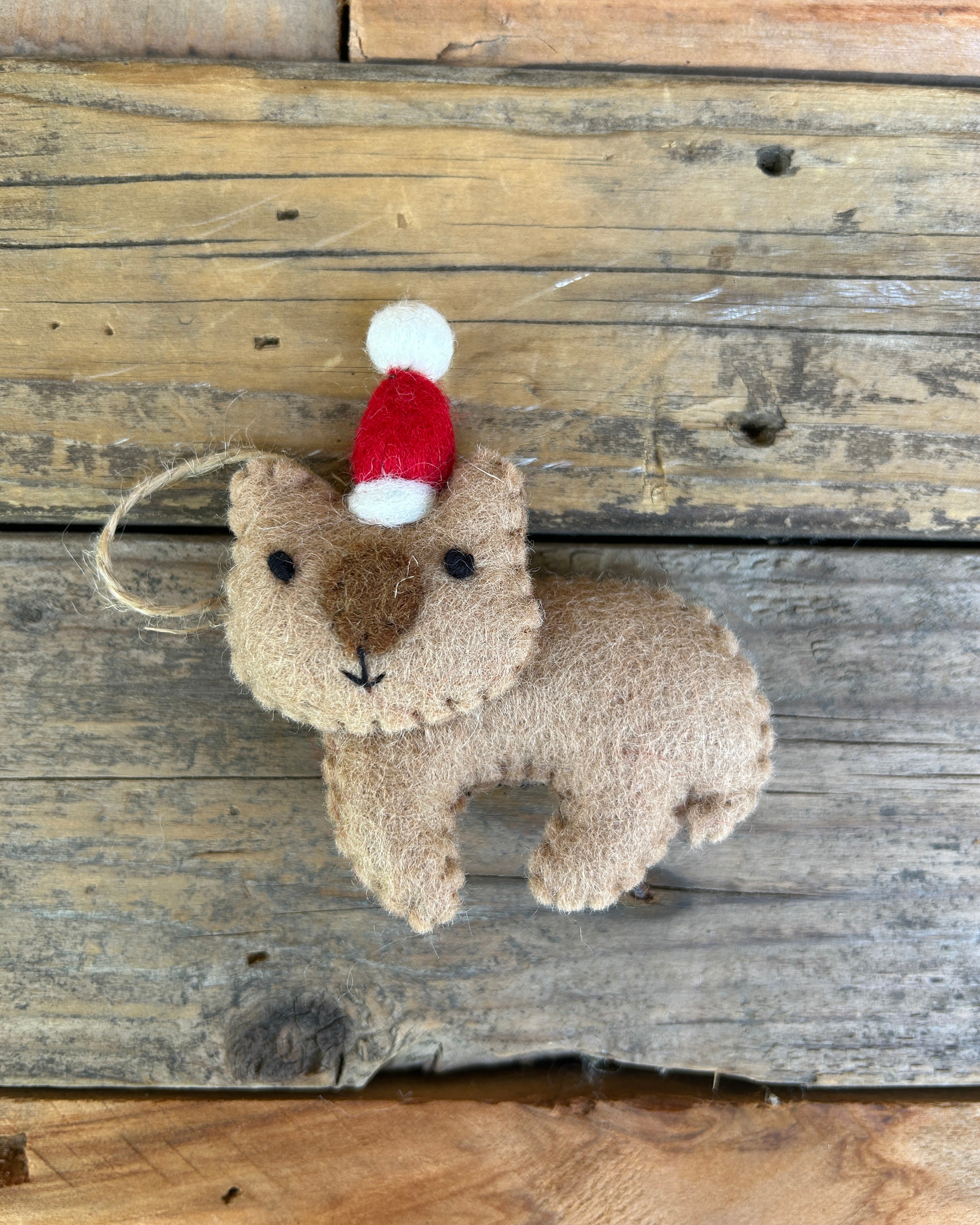 Felted wombat ornament with a red and white hat on a wooden surface