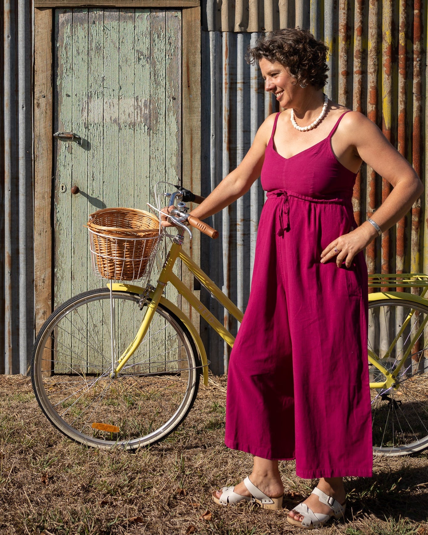 A person wearing a pink romper with a shirred elastic back and adjustable length straps, standing next to a yellow bicycle.