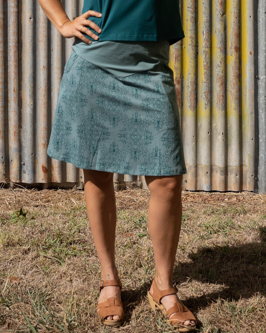 Woman standing under a yellow umbrella with a white fringe against a corrugated metal wall.