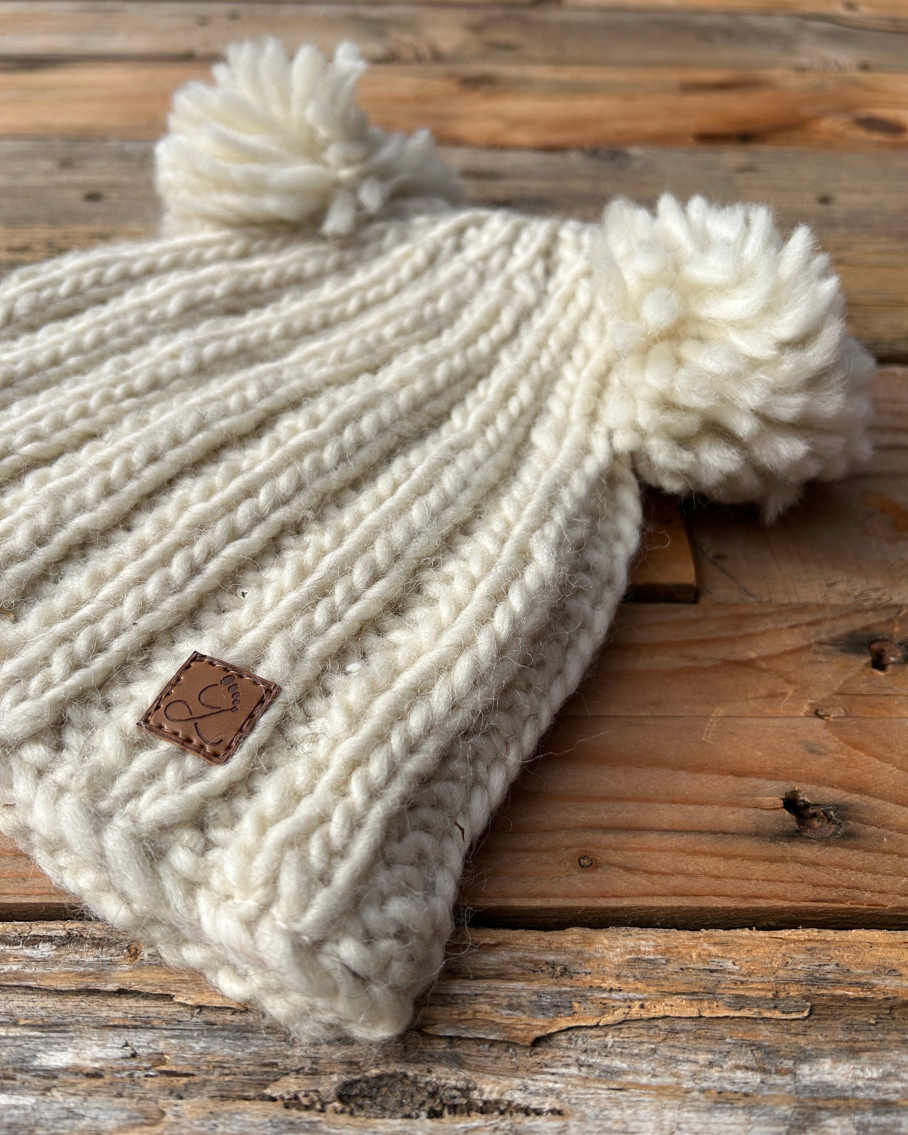 White knitted beanie with pom-poms on a wooden surface
