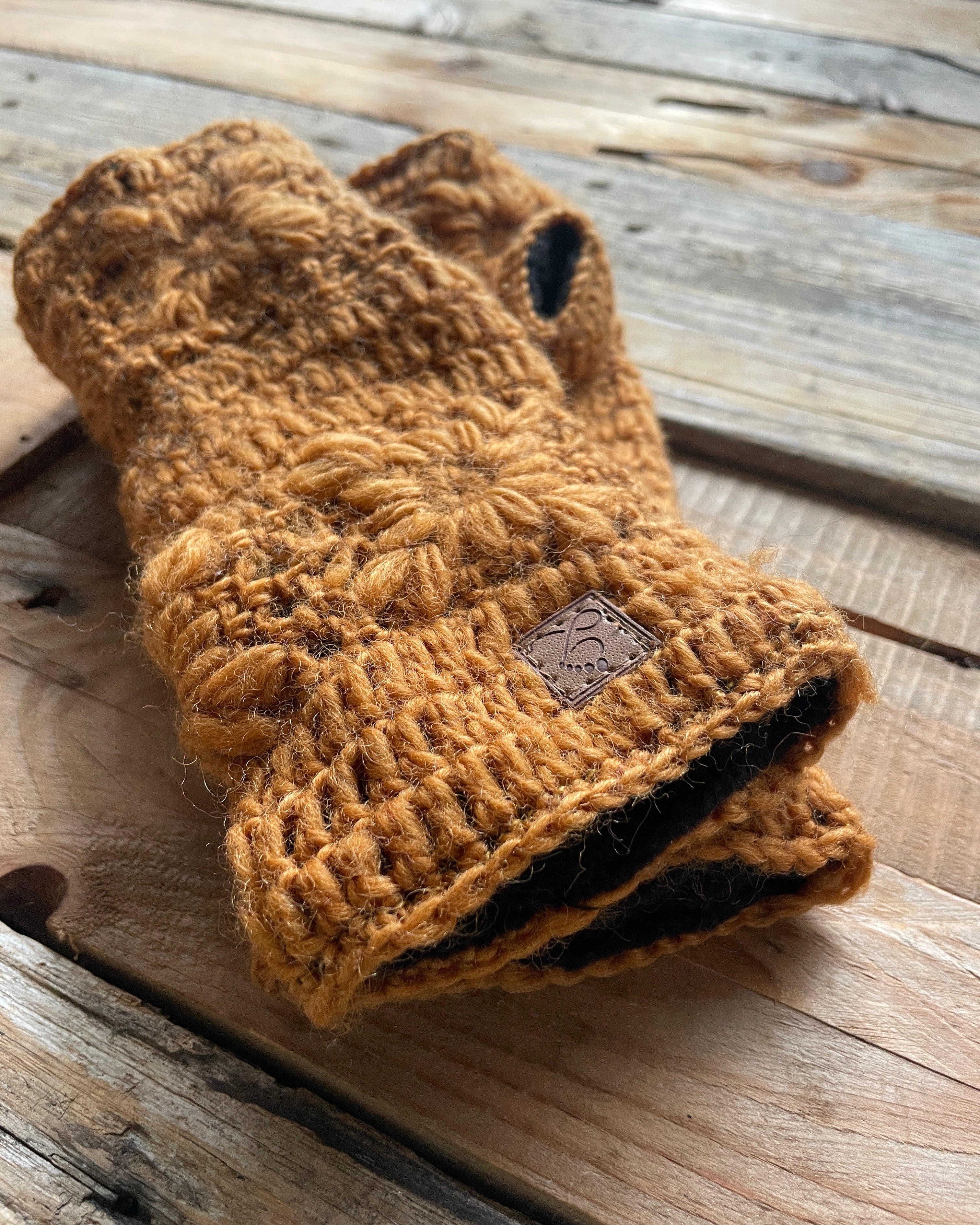 Pair of brown kcrochet wristwarmers on a wooden surface