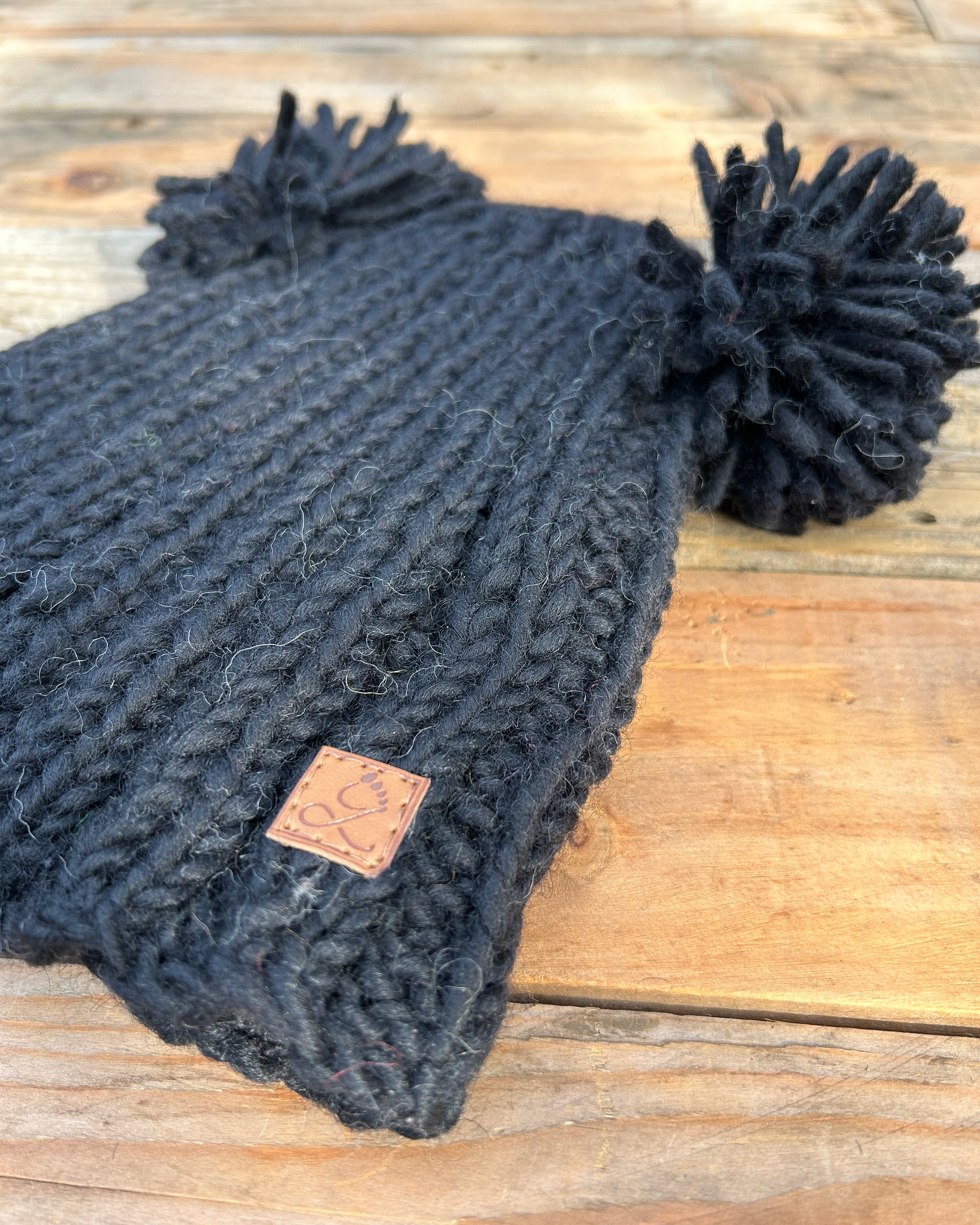 Dark gray knit beanie with pom-poms on a wooden surface