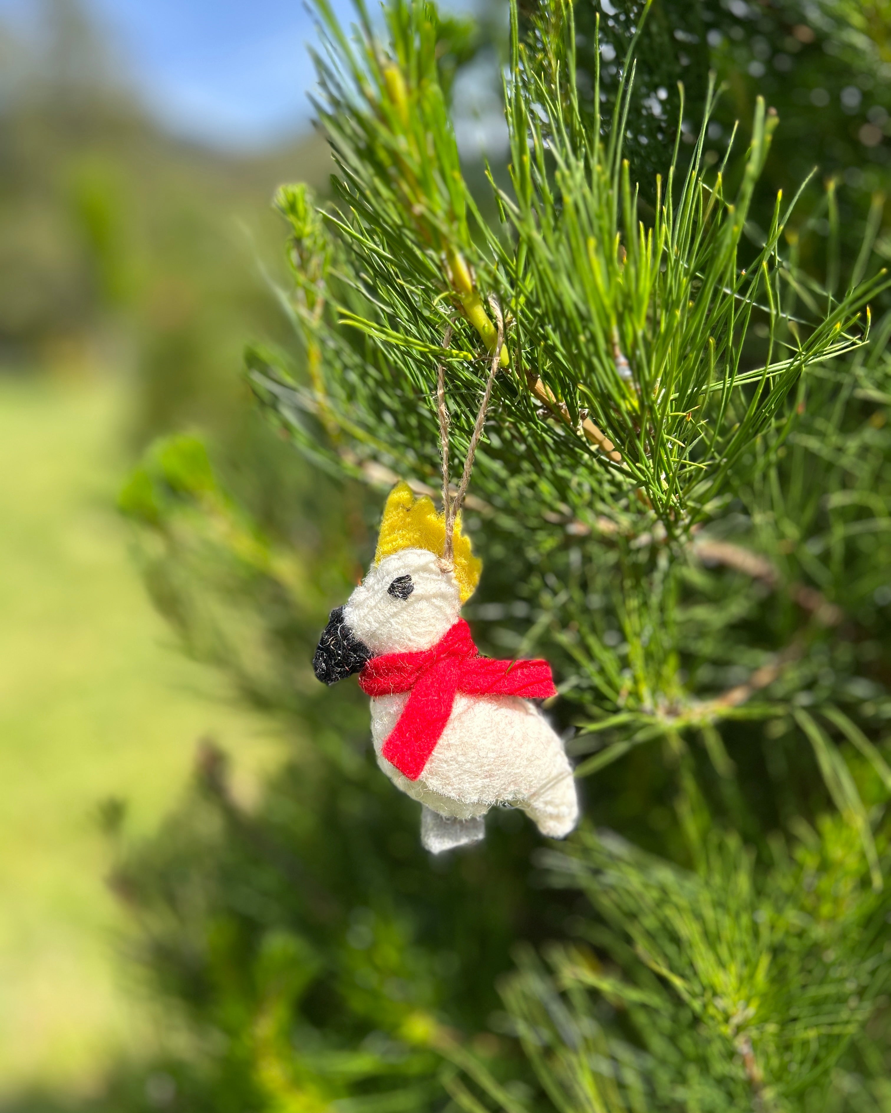Decorative cockatoo ornament with a red scarf and yellow top hat hanging from a tree.