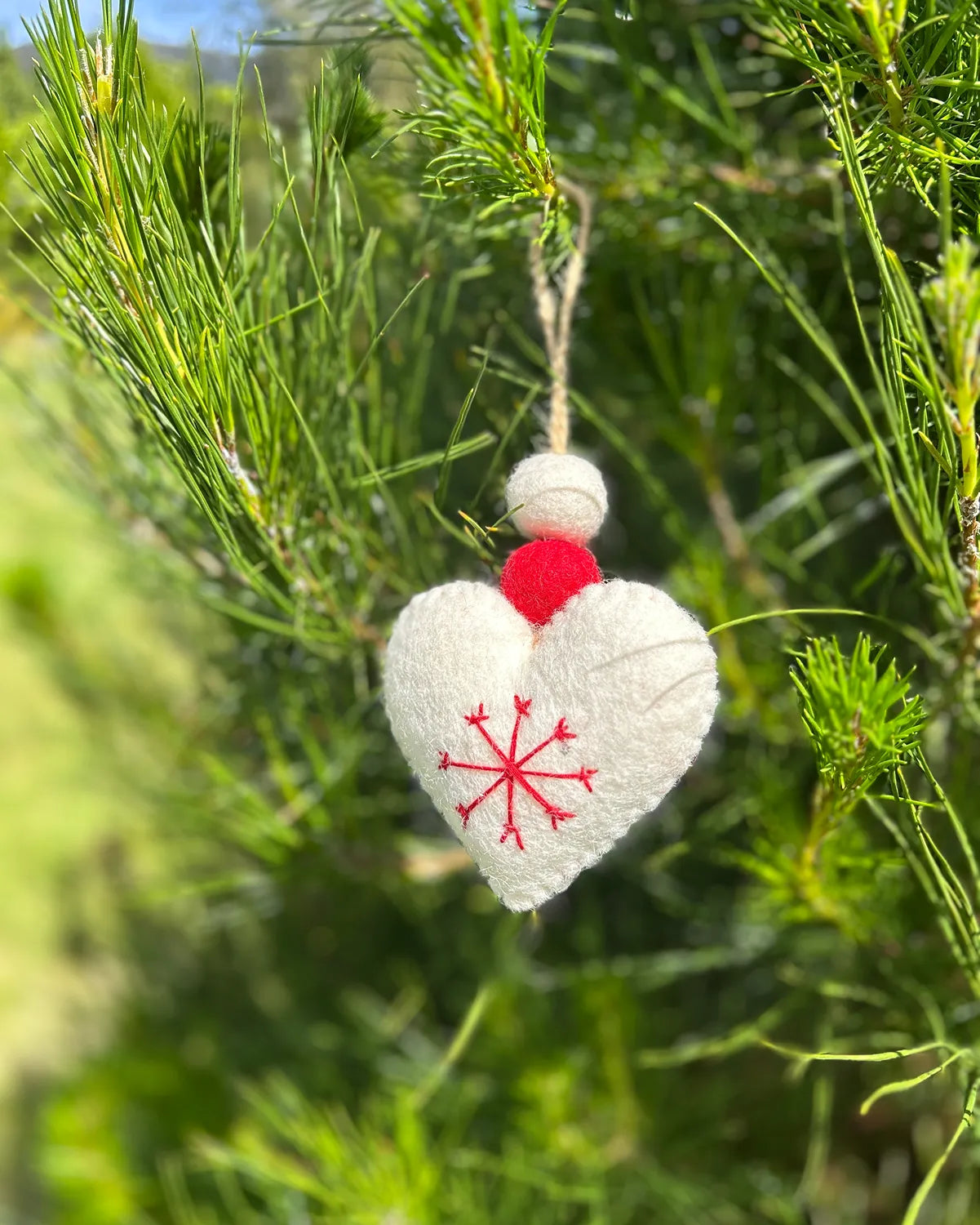 Heart-shaped ornament with red snowflake design hanging from a tree