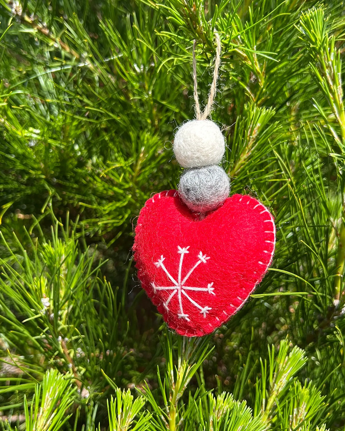 Red heart ornament with red snowflake design hanging from a tree.