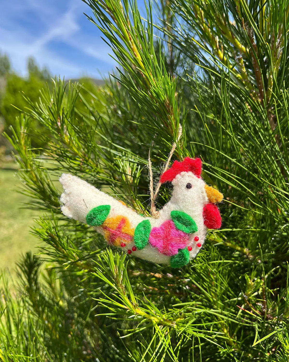 Decorative chicken ornament with colorful feathers hanging in a tree.