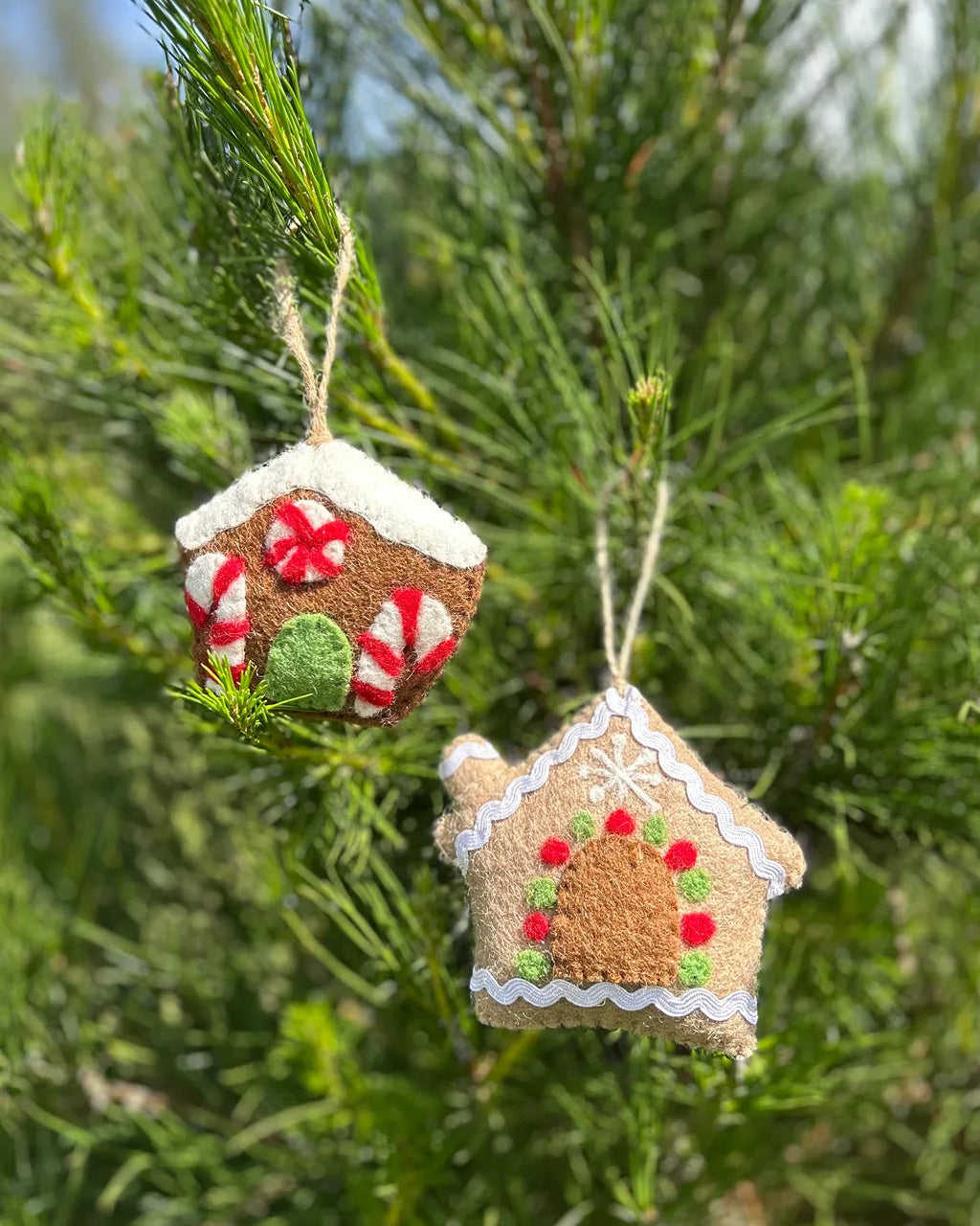 Two gingerbread house ornaments hanging on a Christmas tree.