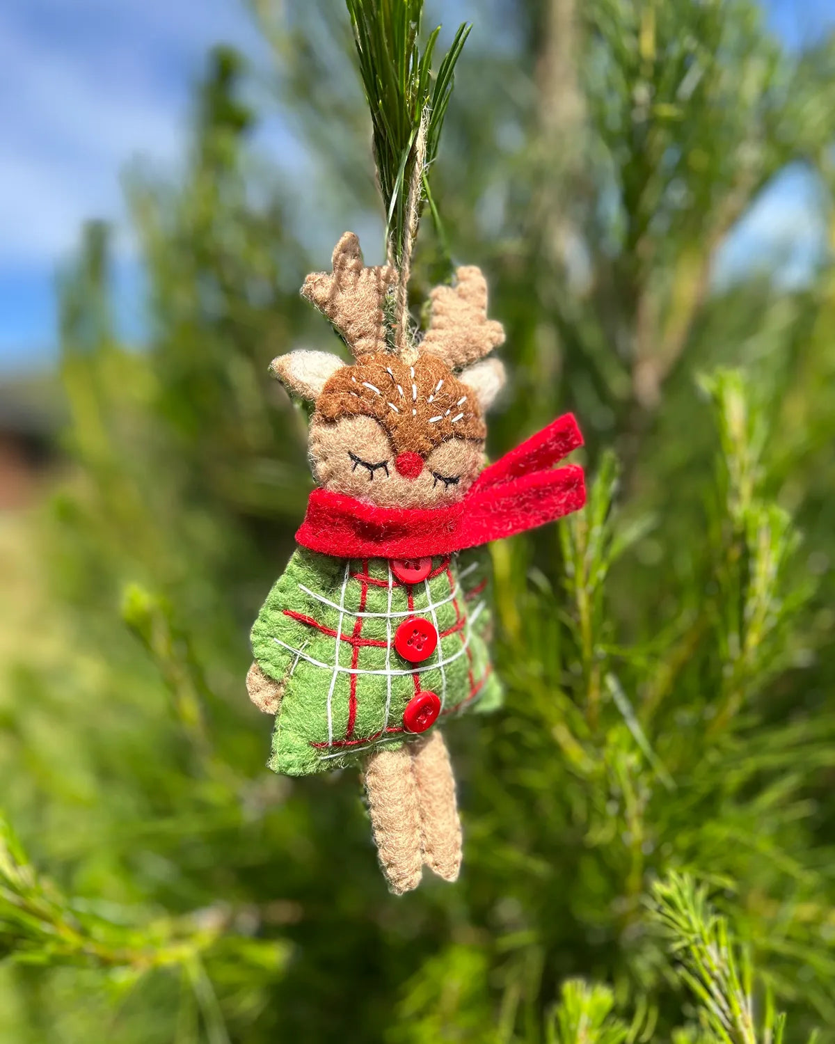 Decorative reindeer ornament with a red scarf and green dress hanging on a tree.