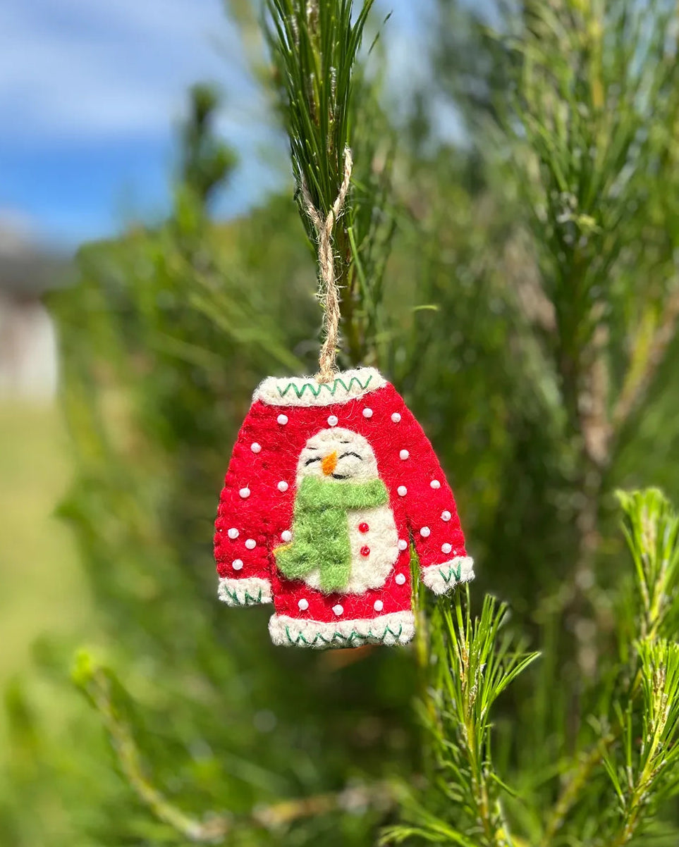 Decorative ornament of a red sweater with a snowman on hanging on a tree.