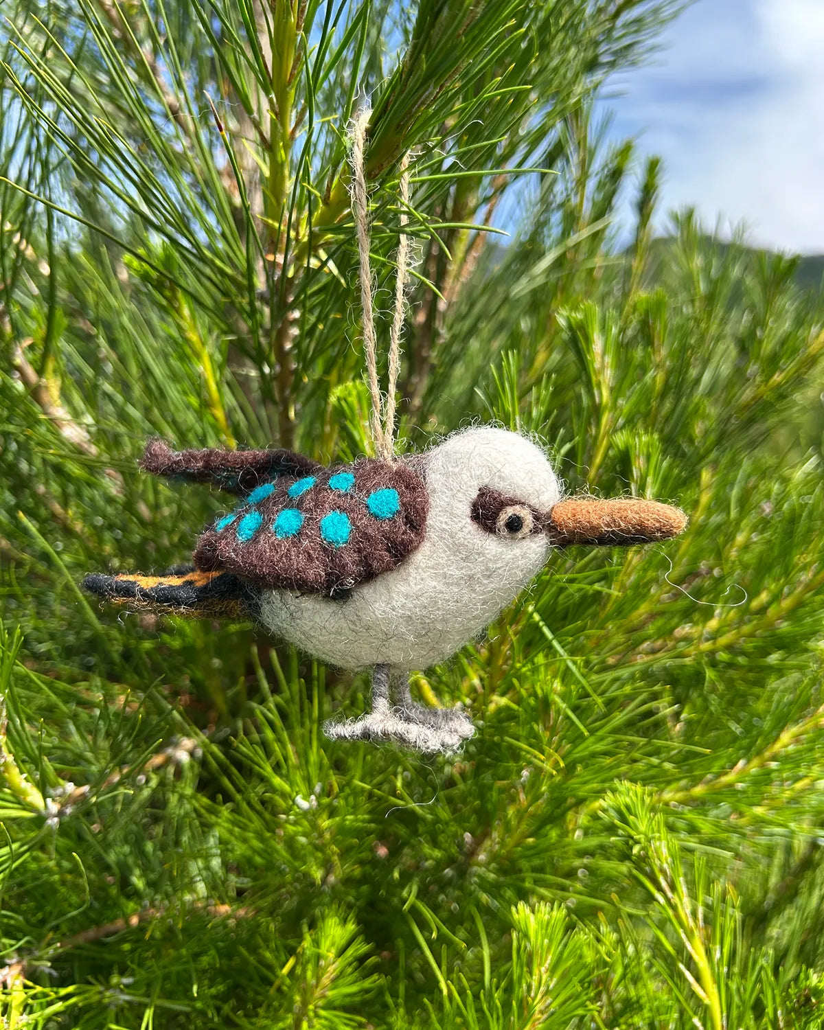 Felted bird ornament hanging from a pine tree