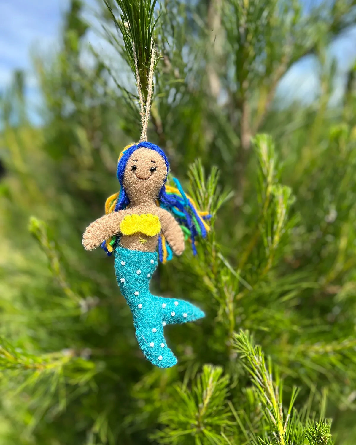 Mermaid ornament with blue tail and yellow top hanging on a tree