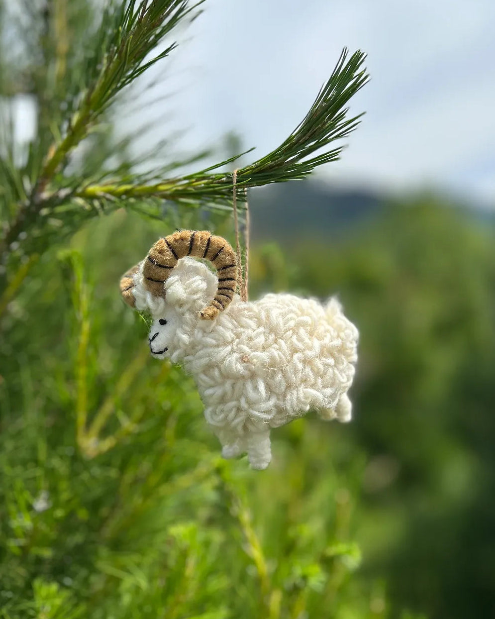 White sheep ornament with brown horns hanging from a tree branch