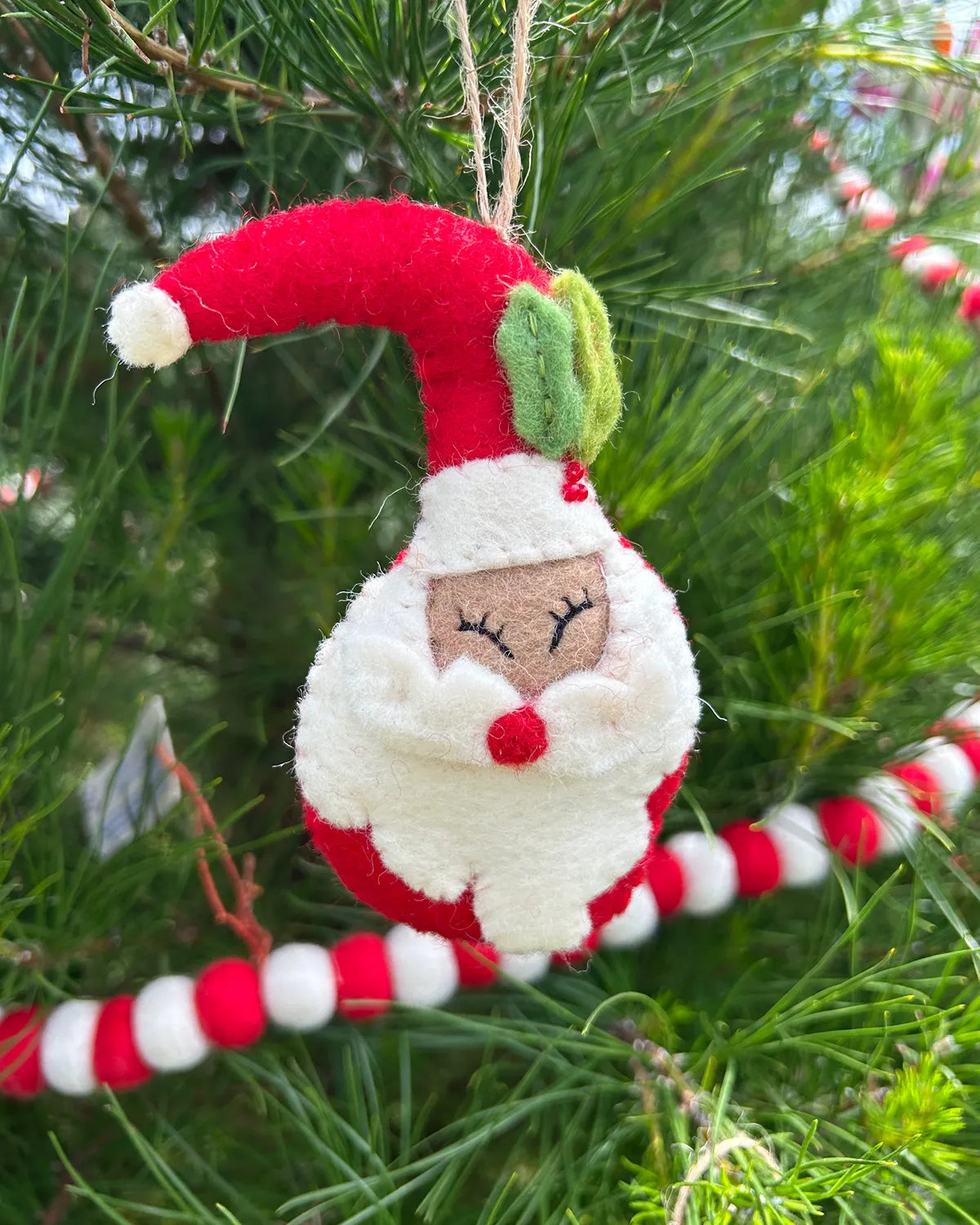 Decorative Christmas ornament Santa shaped like a face with a red hat and white beard, hanging on a tree.