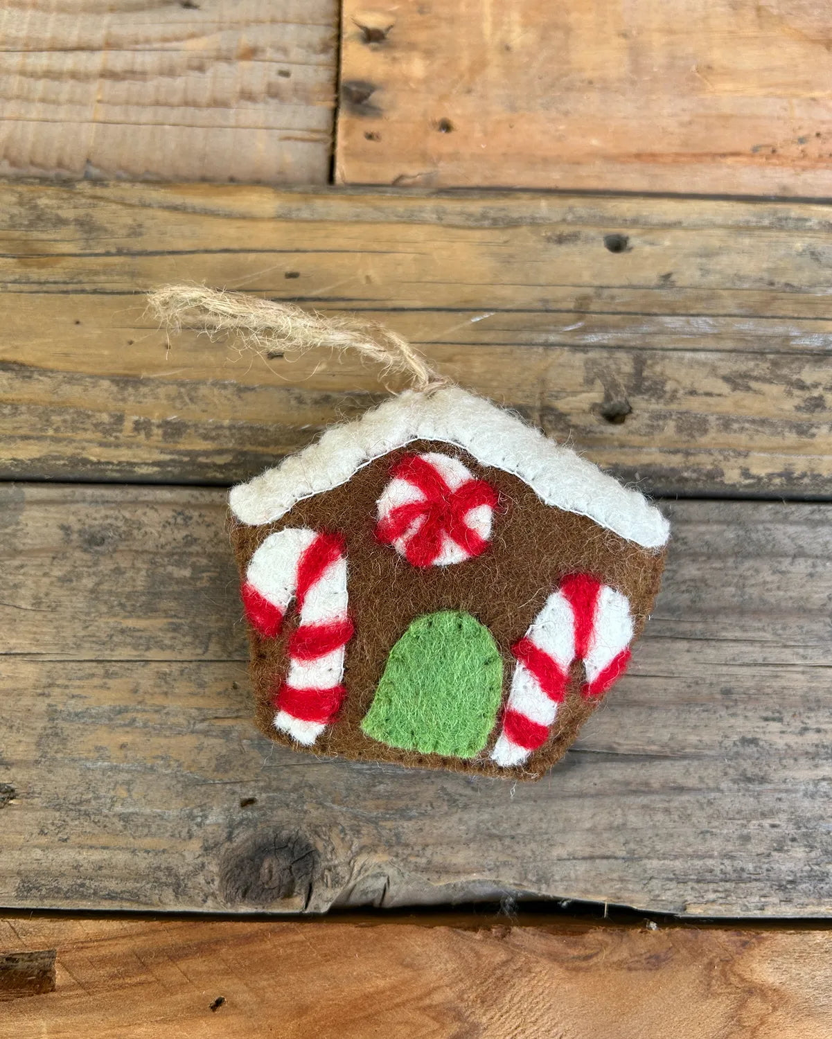 Gingerbread house ornament with candy cane details on a wooden surface