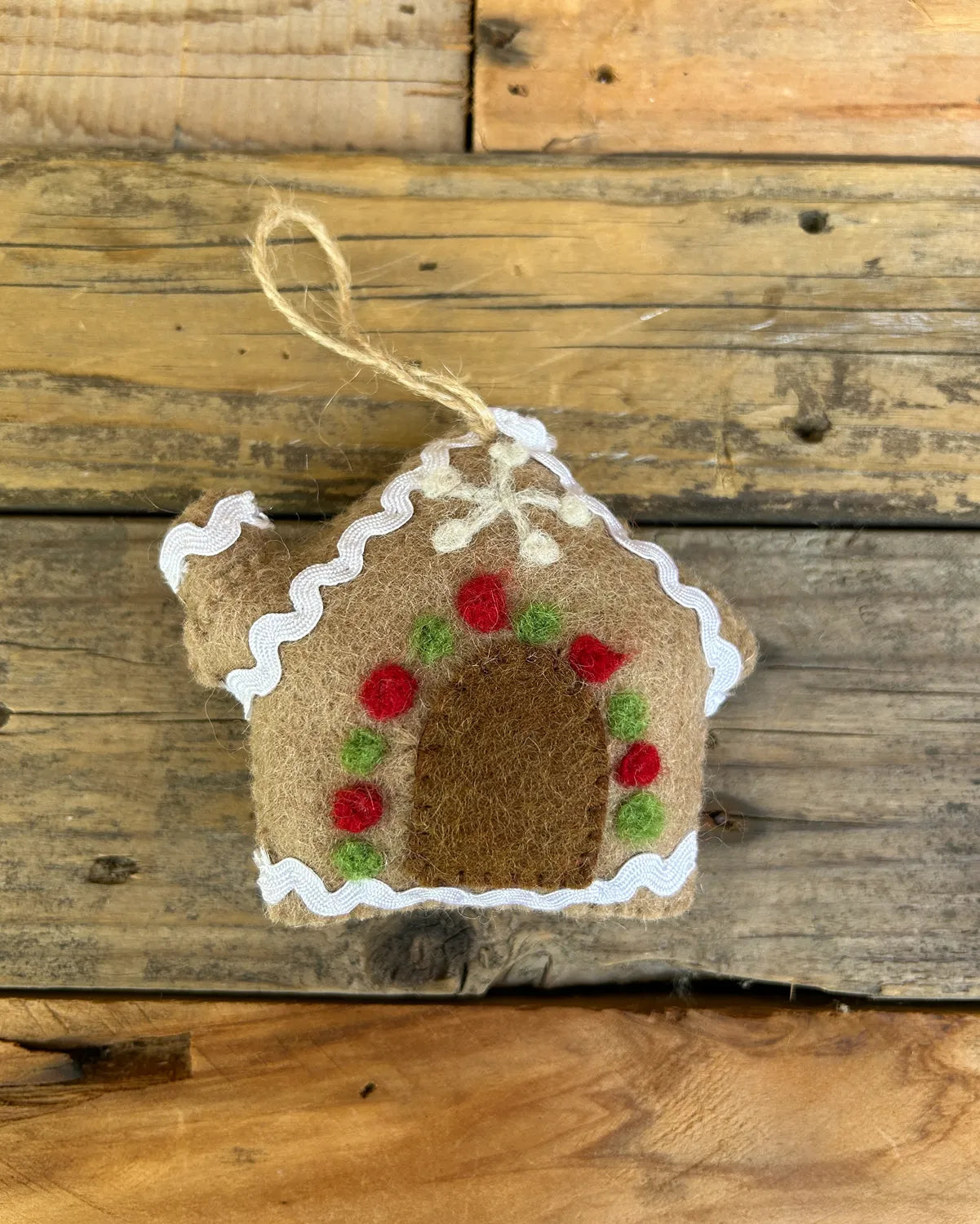 Decorative gingerbread house ornament with red and green details on a wooden background