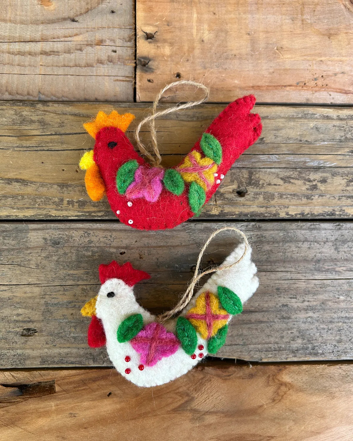 Two felt rooster ornaments on a wooden surface