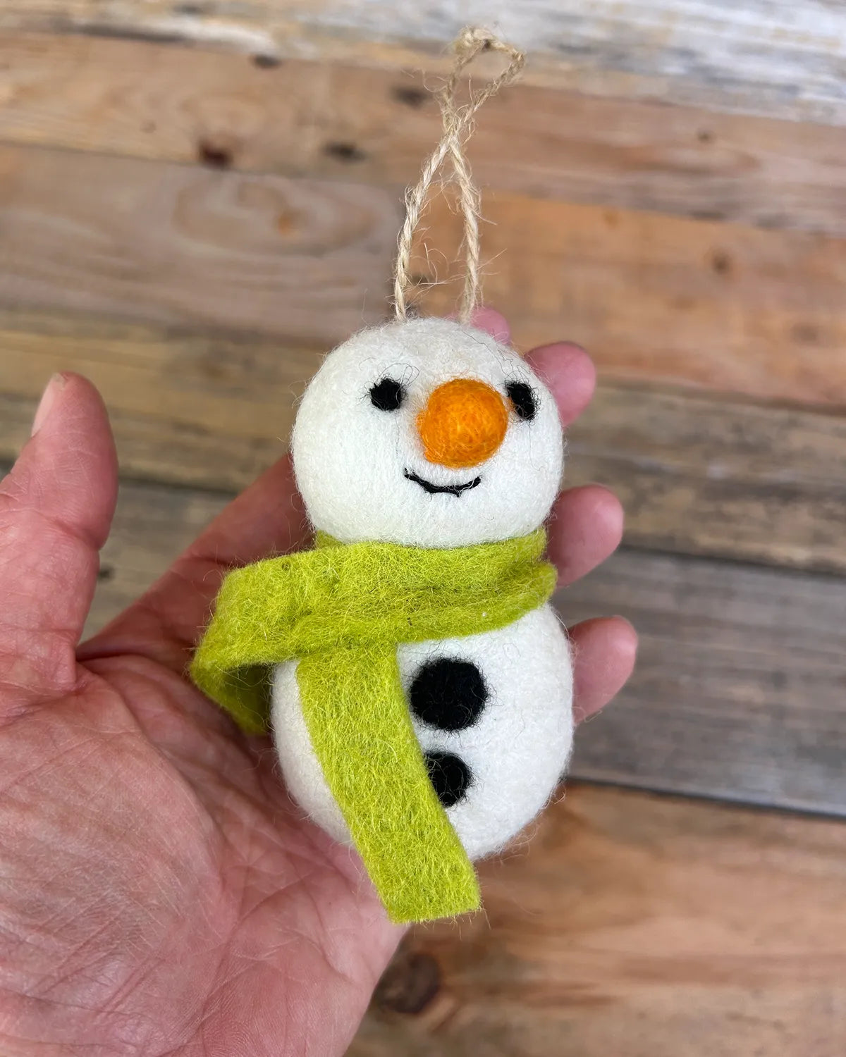 Felted snowman ornament with a green scarf hanging from a tree.