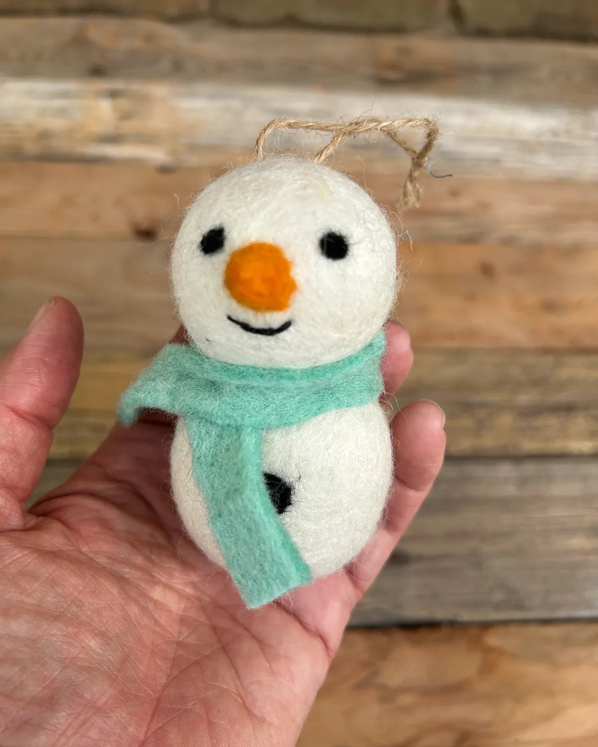 Small snowman ornament with a blue scarf held in a hand against a wooden background