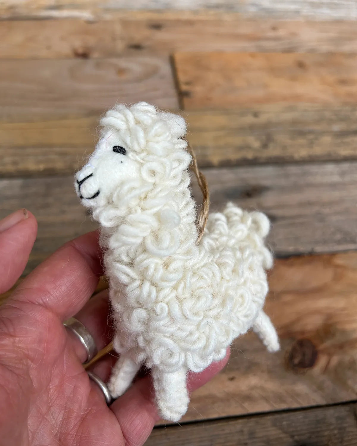 White knitted llama toy held in a hand against a wooden background