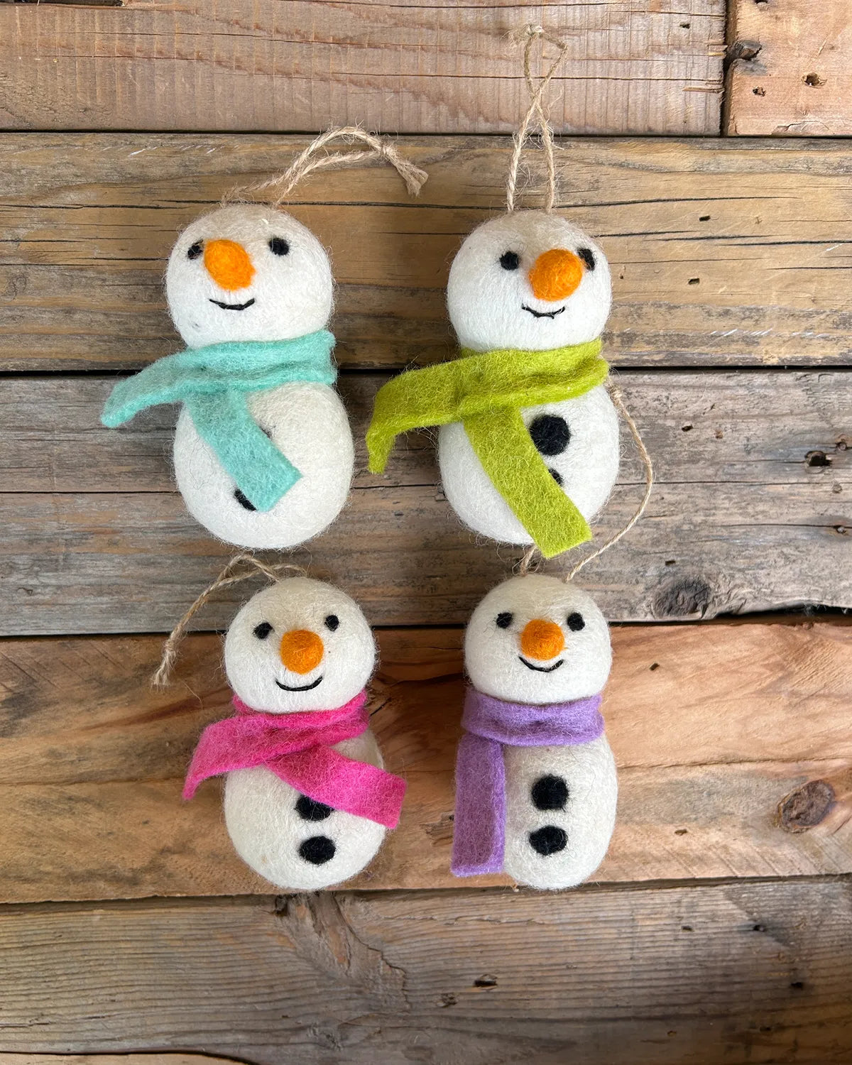 Four felt snowman ornaments with colorful scarves on a wooden background