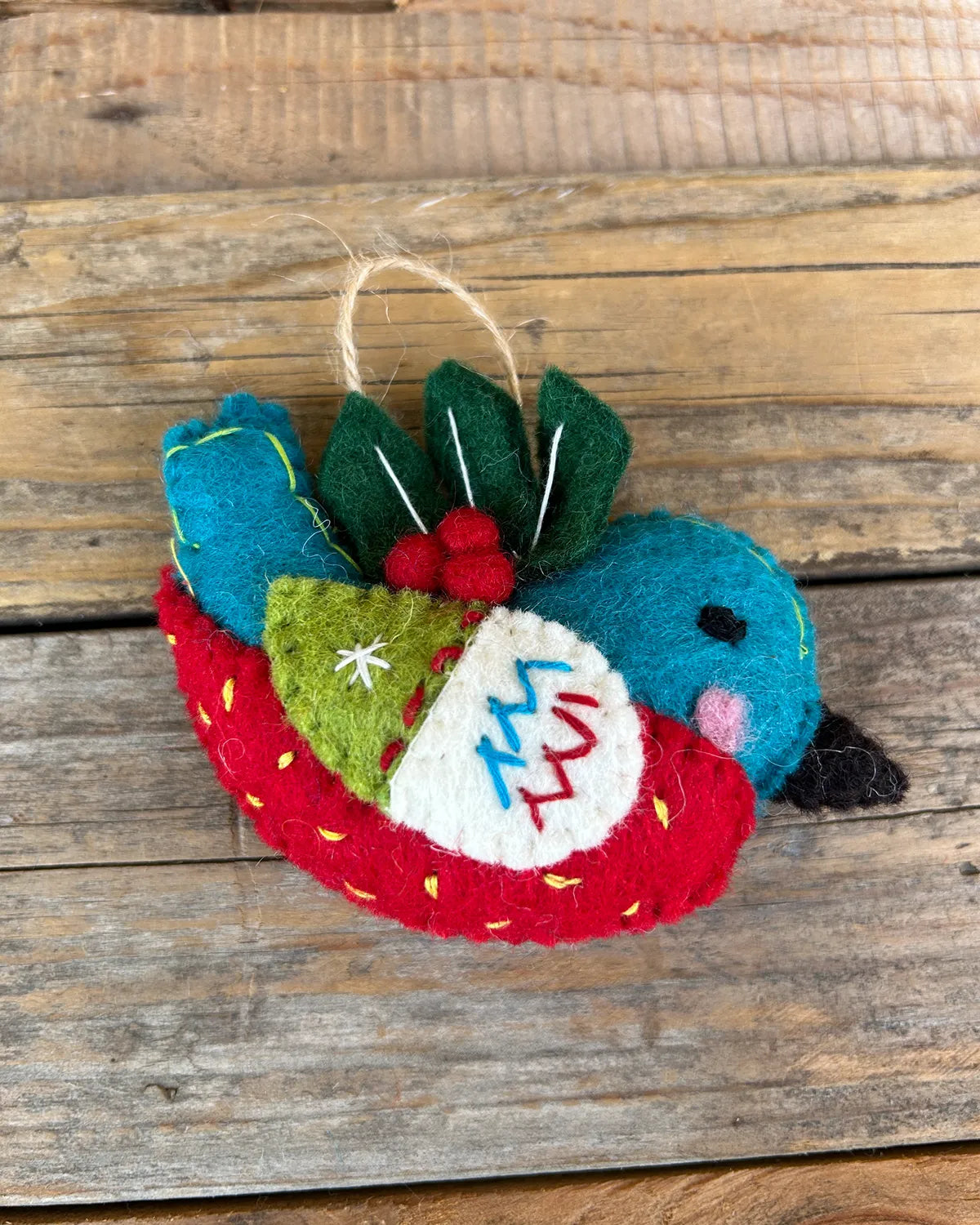 Felt ornament shaped like a bird with red and green accents on a wooden surface