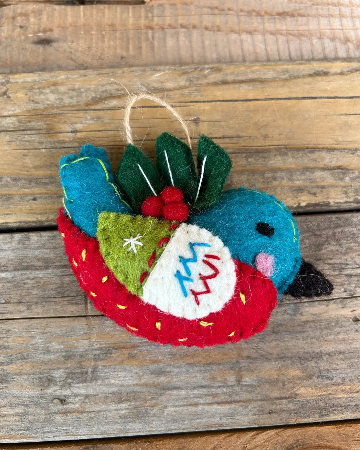 Felt ornament shaped like a bird with red and green accents on a wooden surface