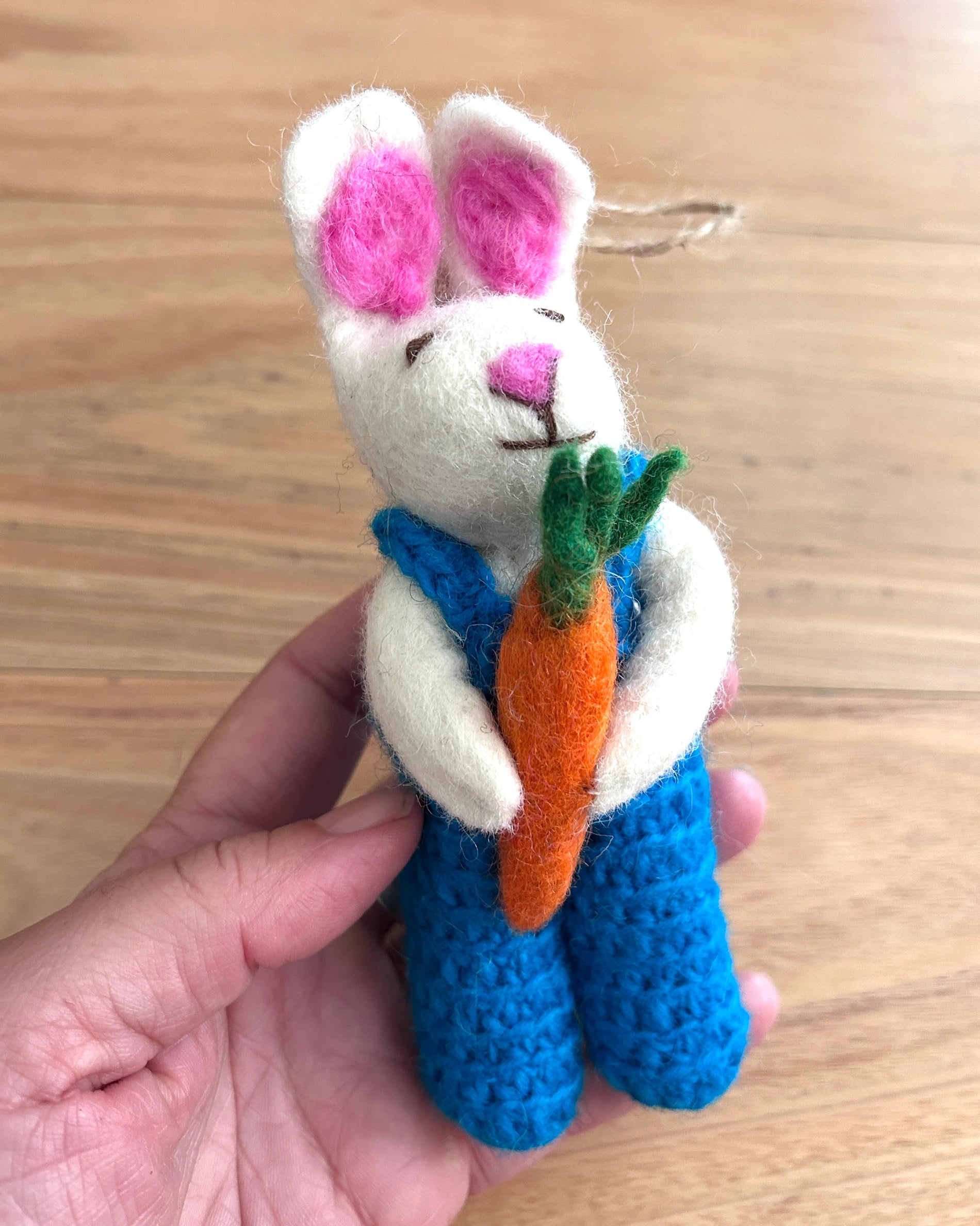 Handmade felt rabbit toy with a carrot held by a person on a wooden surface