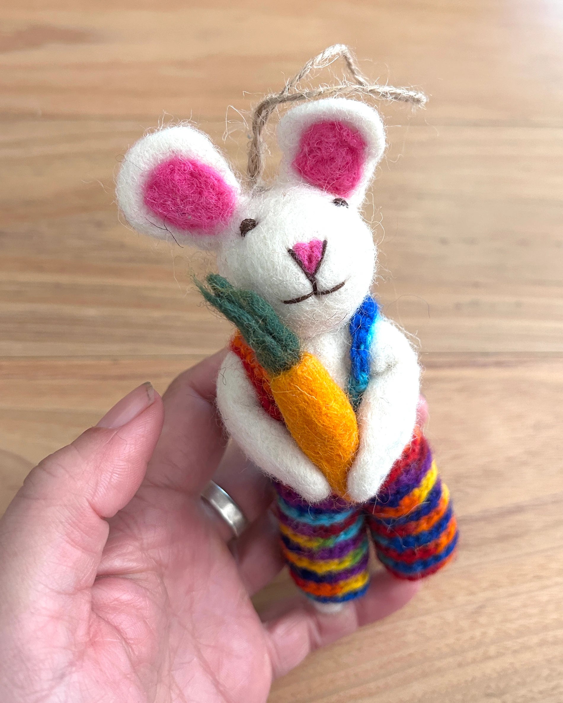 Handmade plush bunny toy with colorful scarf and carrot held by a hand on a wooden surface