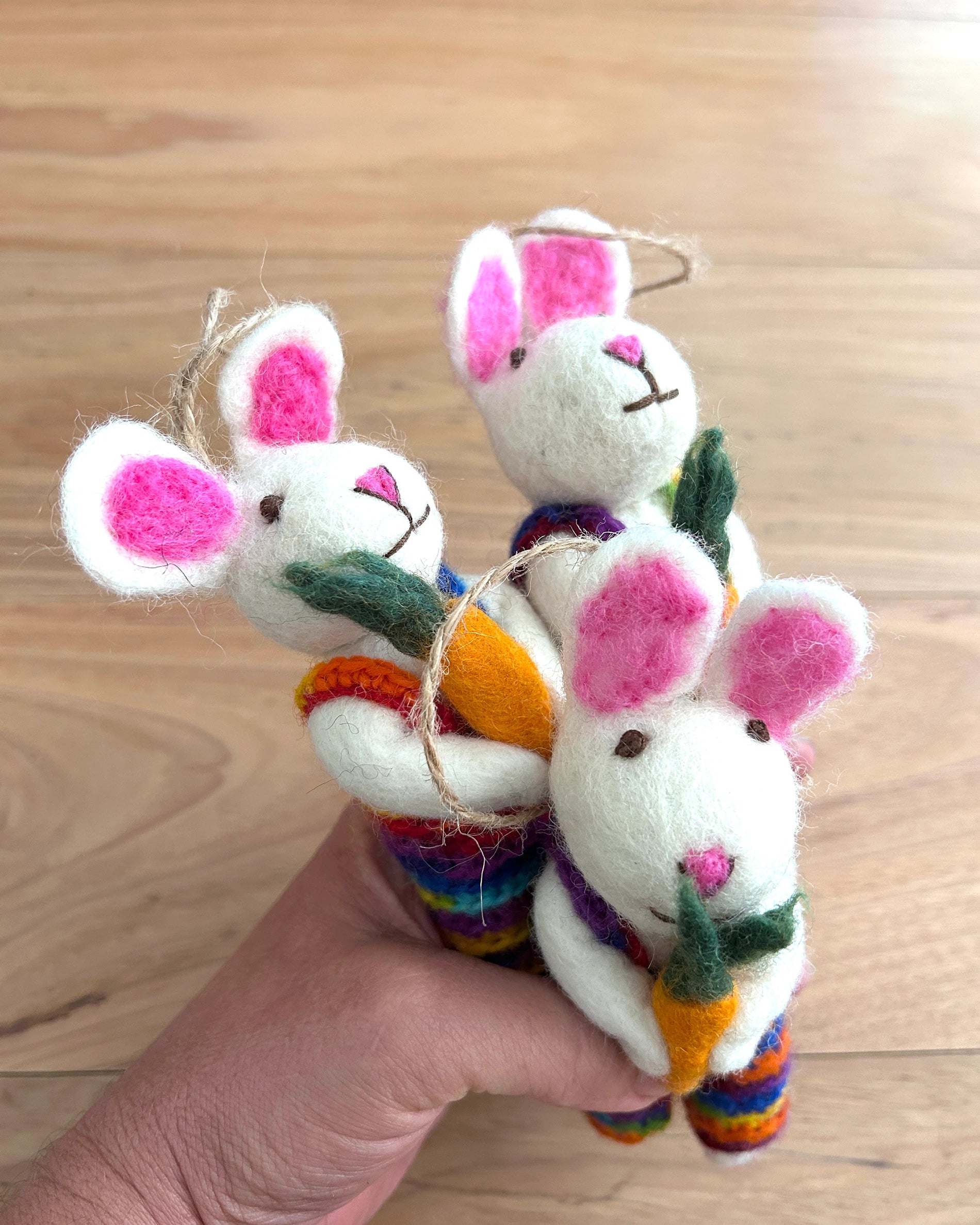 Three small plush toy rabbits with colorful scarves held by a hand on a wooden surface.
