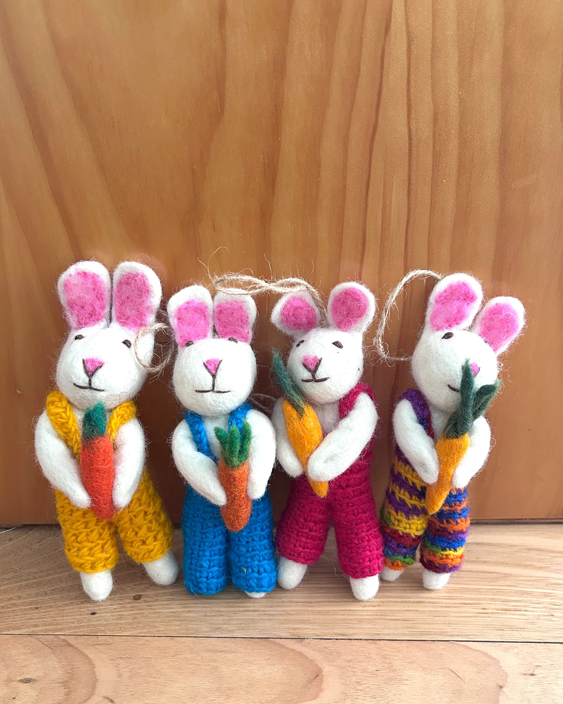 Four colorful knitted bunnies with scarves and carrots on a wooden surface.