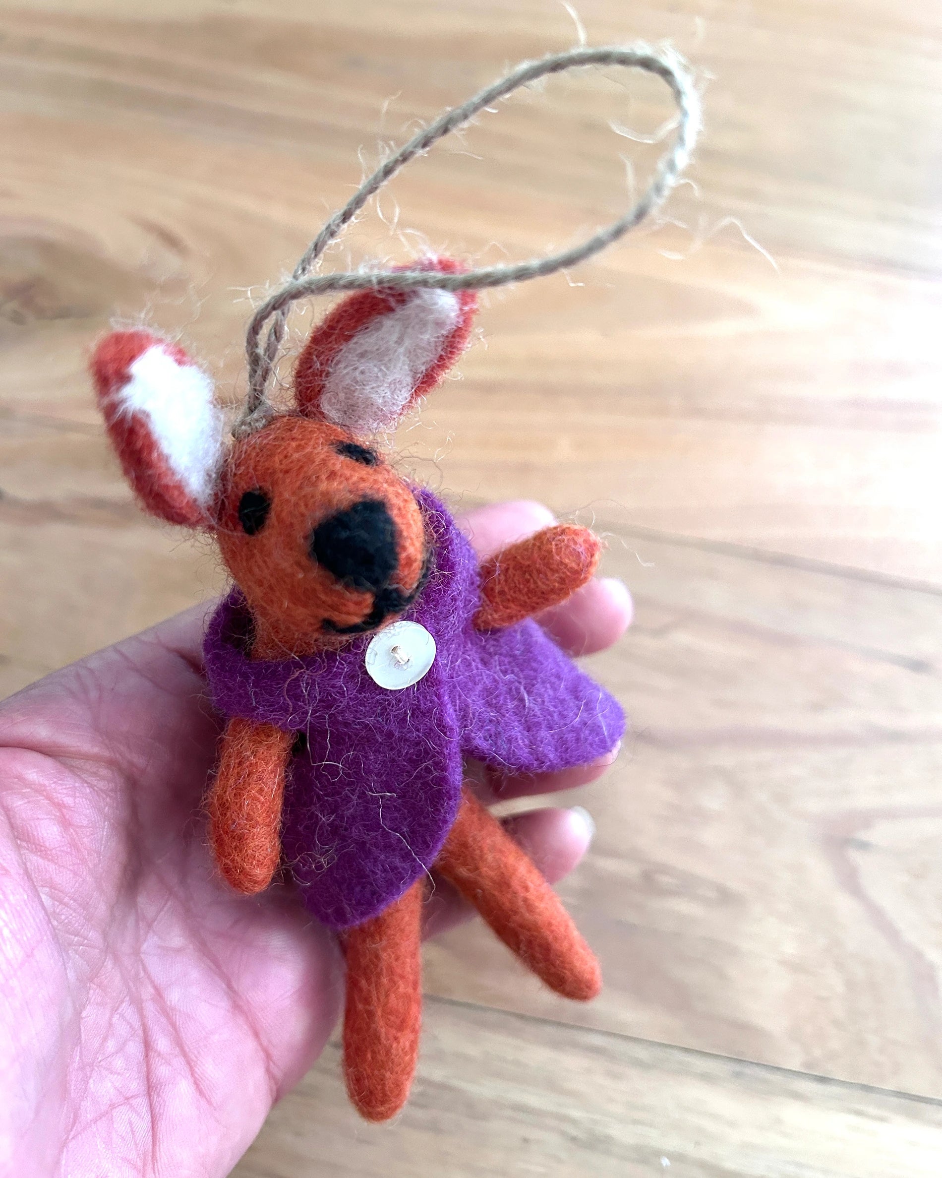 Small orange and purple plush toy held in a hand on a wooden surface