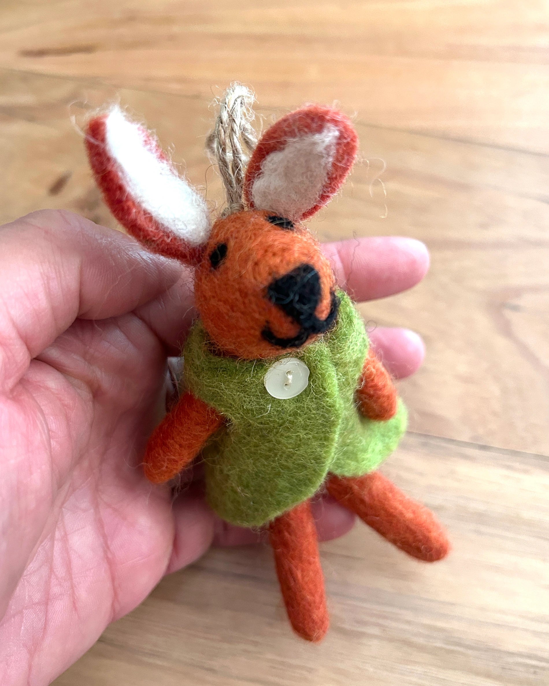 Small felted animal ormament held in a hand on a wooden surface