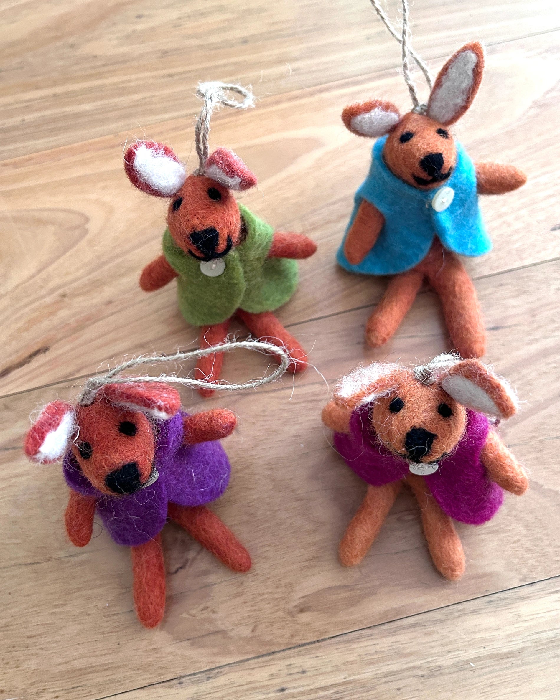 Four felted rabbit keychains on a wooden surface