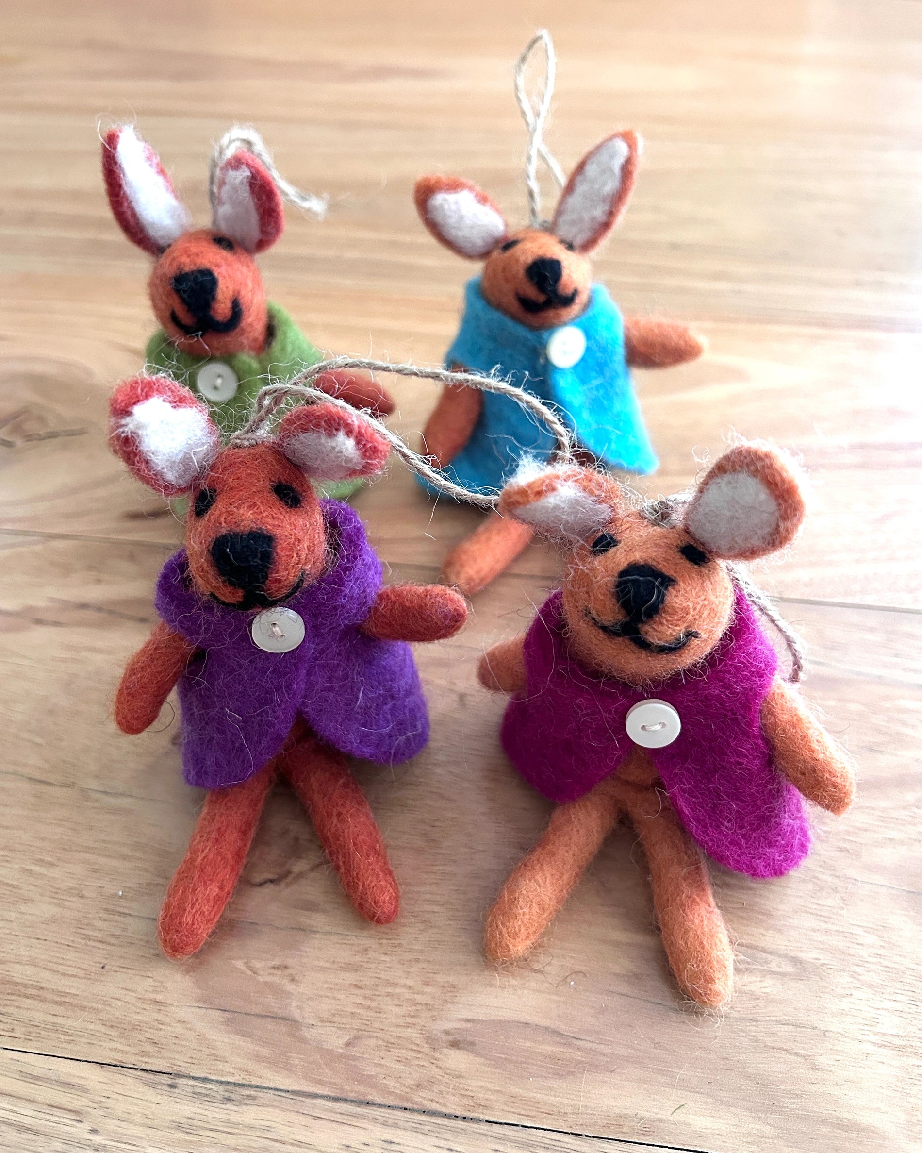Four small stuffed bunny ornaments with colorful clothing on a wooden surface