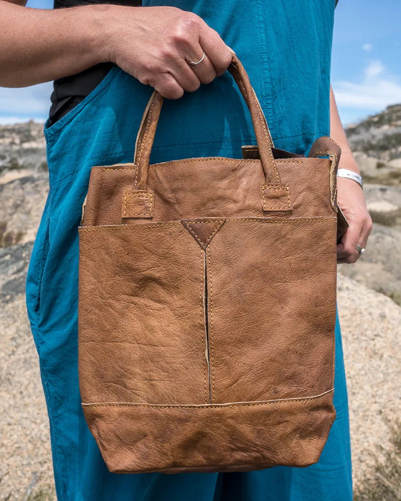 Person holding a brown leather bag in a desert landscape