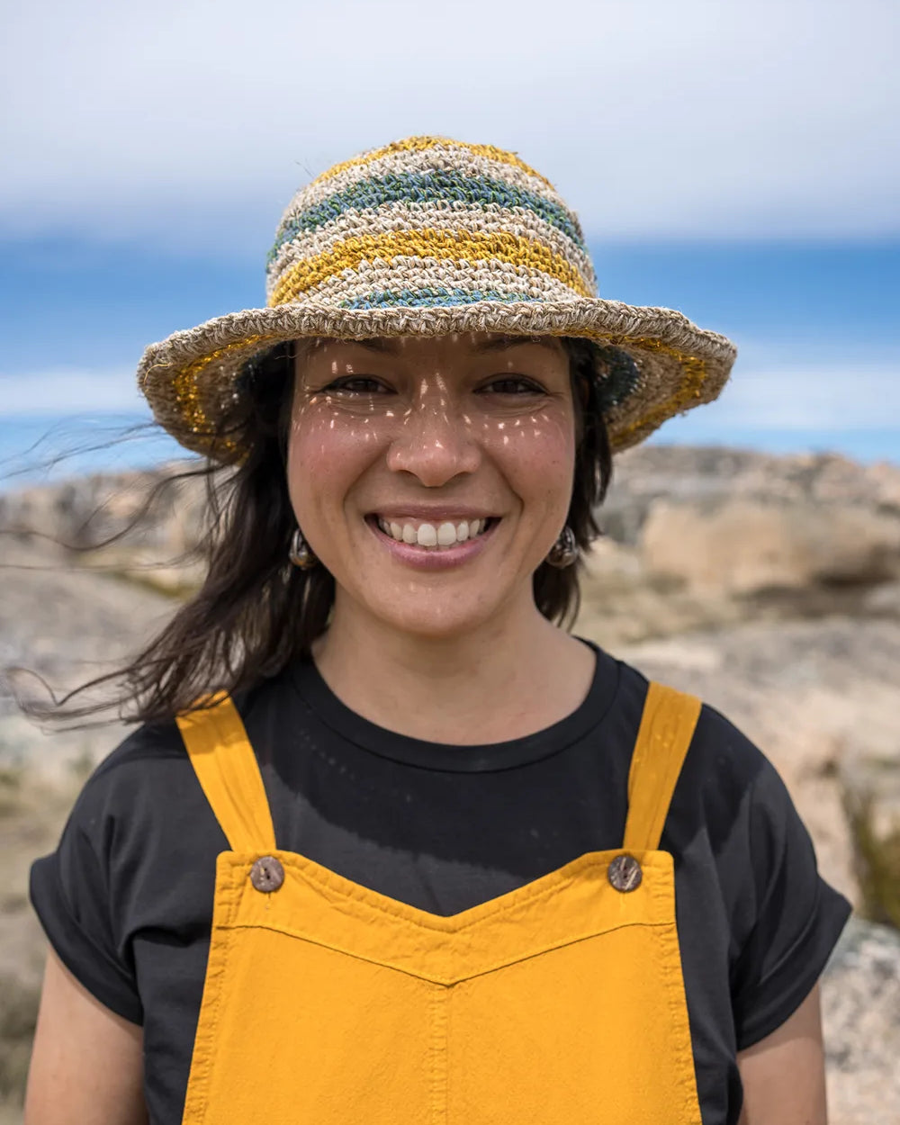 Person wearing a straw hat and yellow overalls standing outdoors with a blue sky background