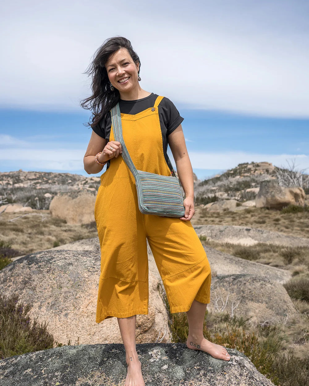 Woman in yellow jumpsuit holding a green bag on a rocky landscape