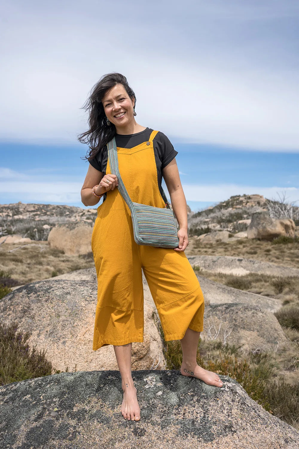 Woman in yellow jumpsuit holding a green bag on a rocky landscape