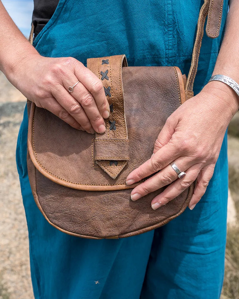 Person holding a brown leather bag outdoors with a natural landscape in the background