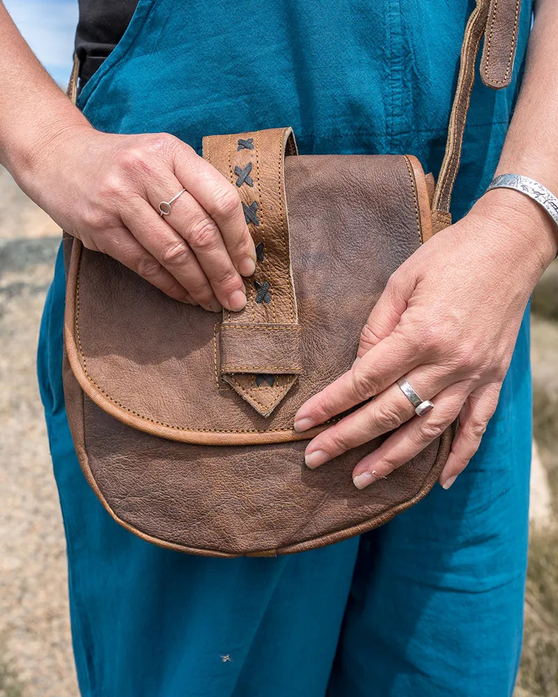 Person holding a brown leather bag outdoors with a natural landscape in the background