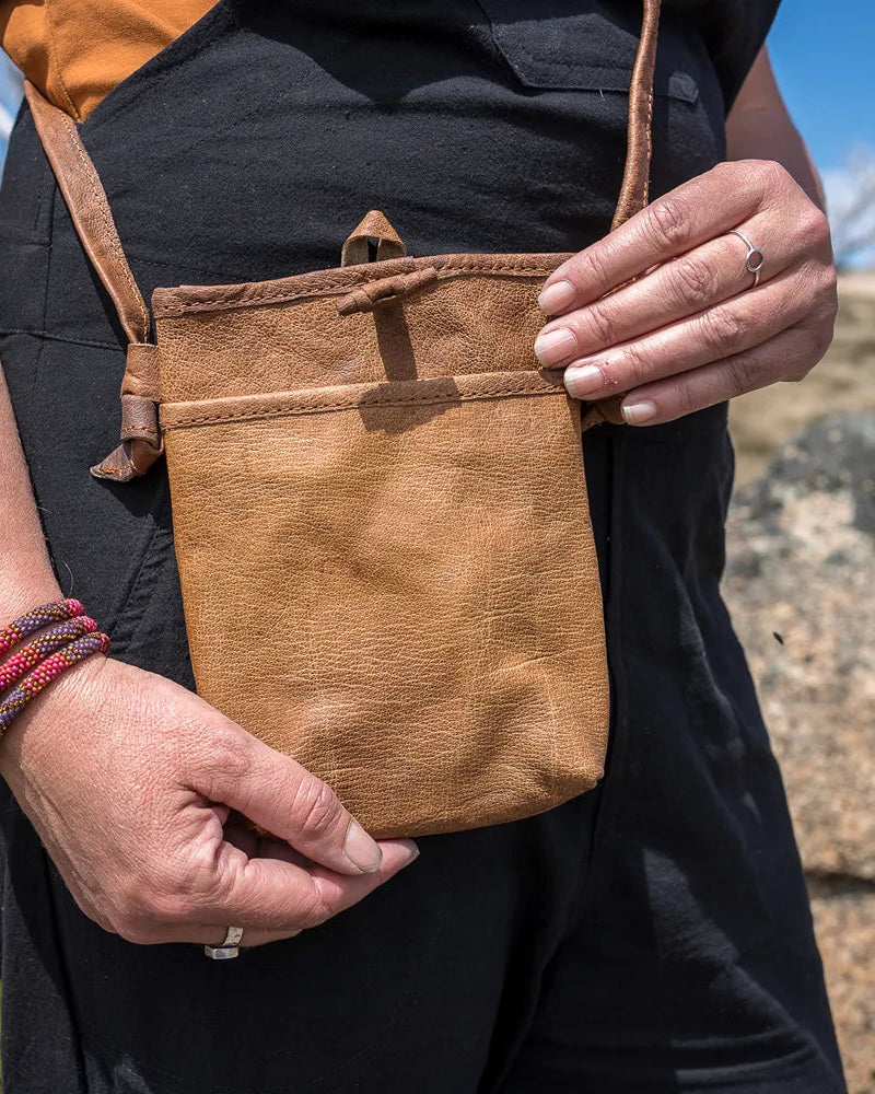 Person holding a brown leather pouch outdoors with a scenic background