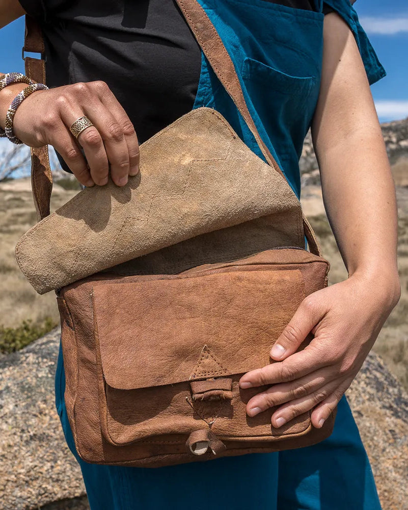 Person holding a brown leather bag in a natural outdoor setting