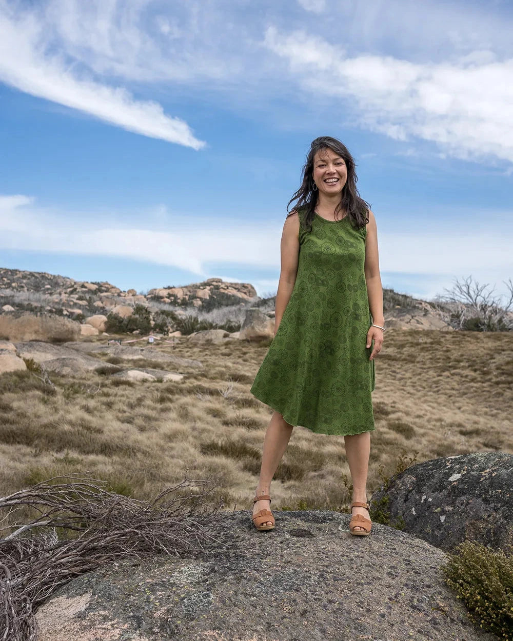 Woman in a green dress standing on a rocky outcrop with a scenic background