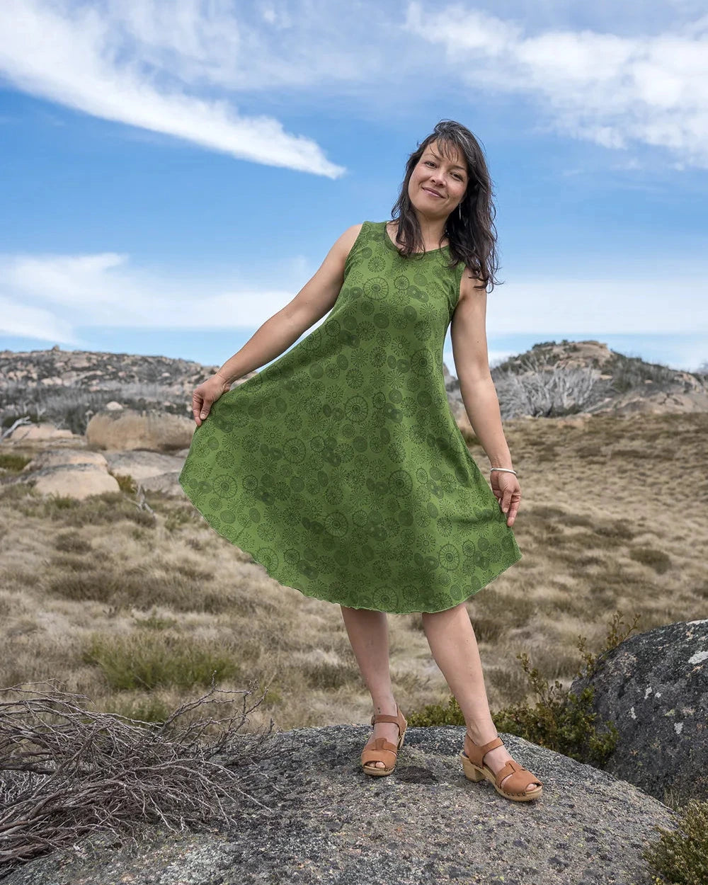 Woman in a green dress standing on a rocky landscape with a blue sky.