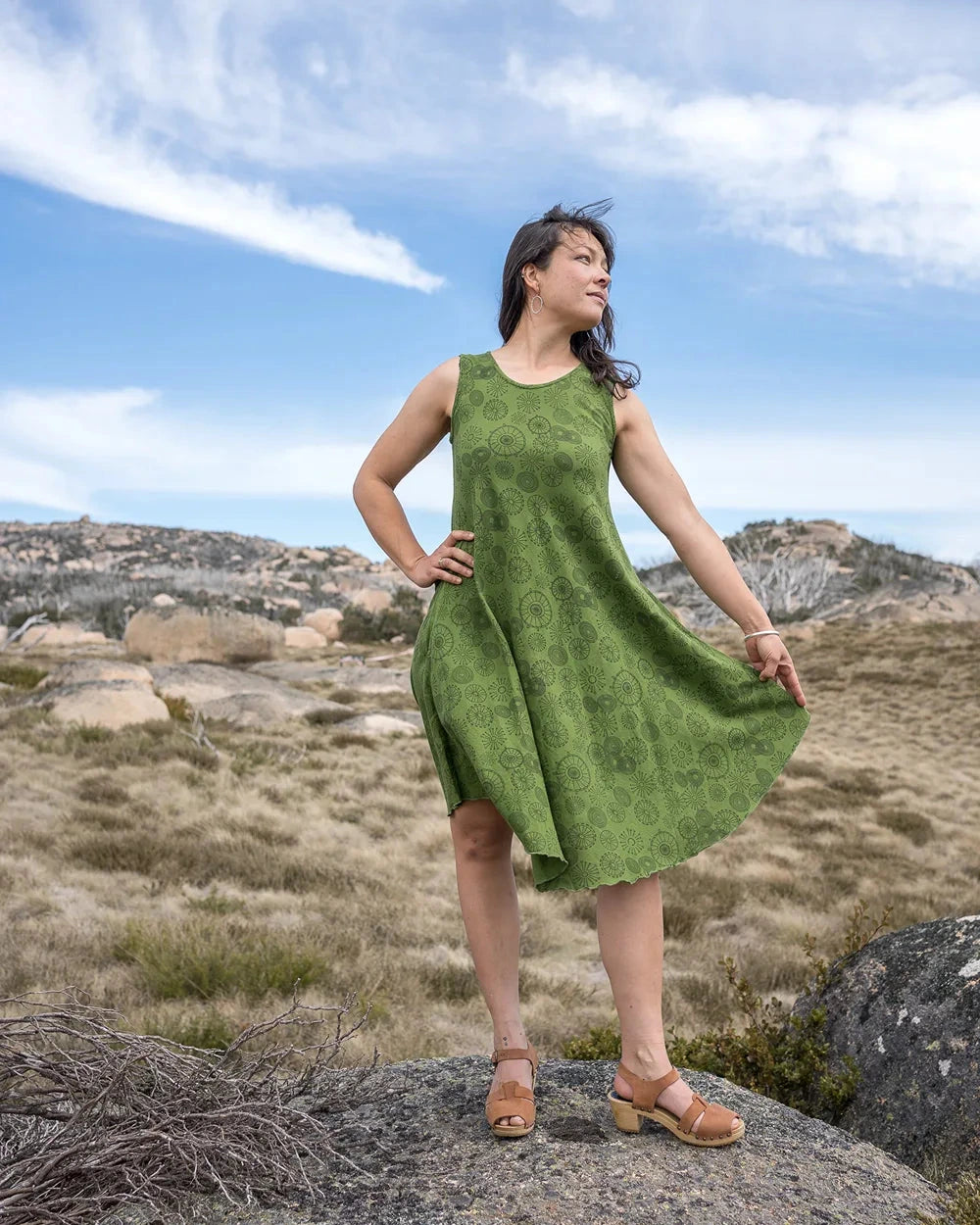 Woman in a green dress standing on a rocky landscape with a blue sky.