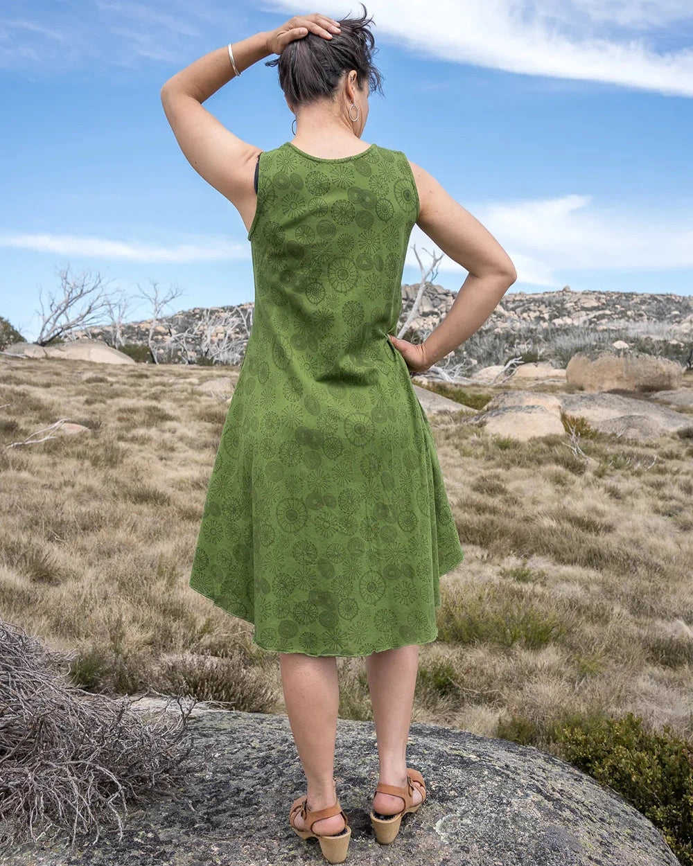 Woman in a green dress standing on a rocky outcrop with a scenic background