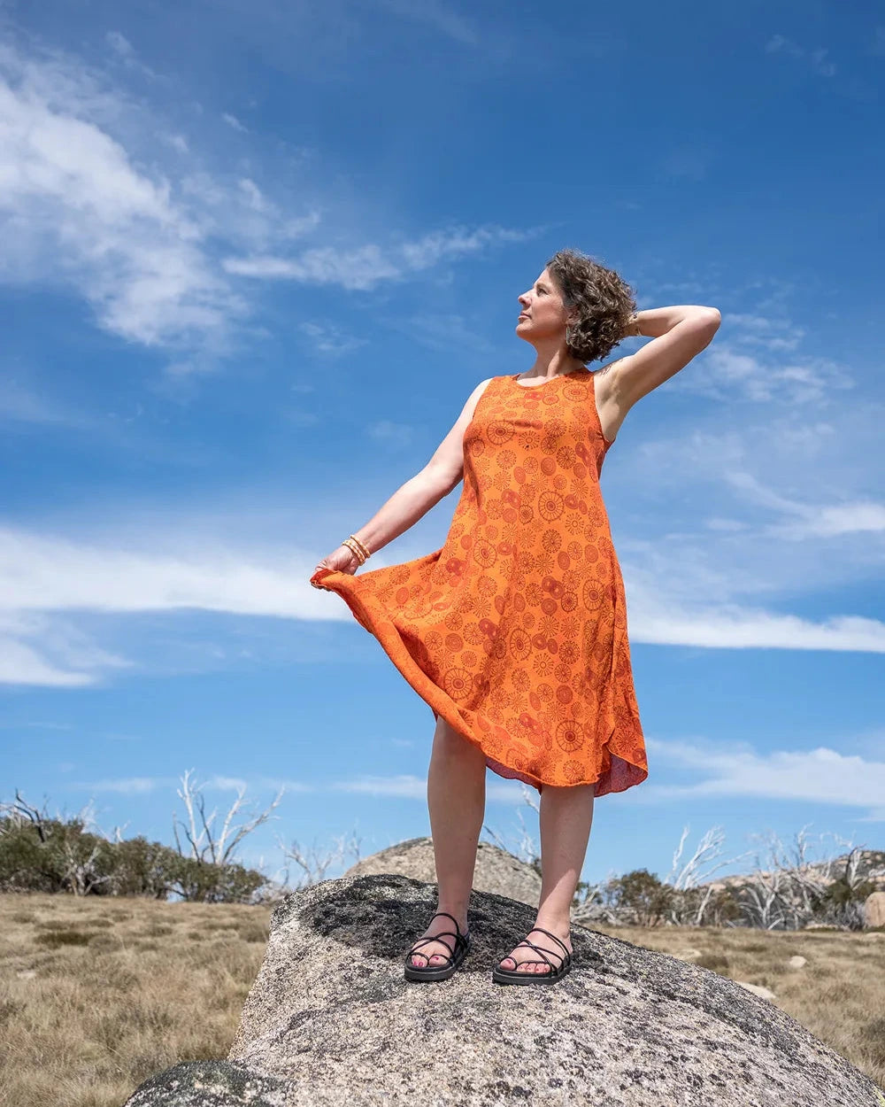 Woman in an orange dress standing on a rock with a blue sky and clouds in the background